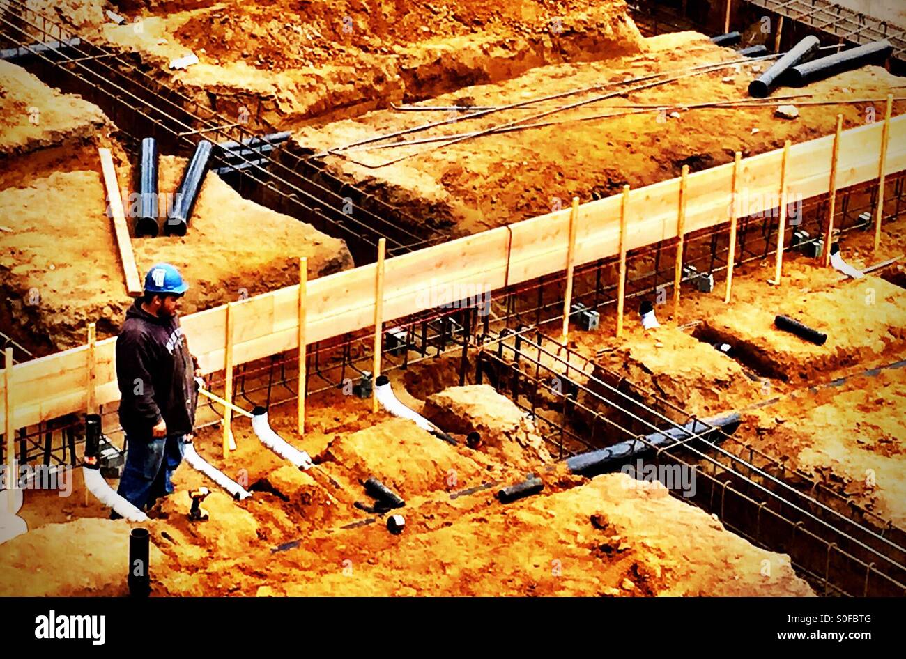 Bauarbeiter überwacht traversierende Infrastruktur, die Kreuz und quer durch die Grundlage für ein neues Wohnprojekt. San Francisco, Kalifornien, USA. - Smartphone-aufgenommenes Stockfoto
