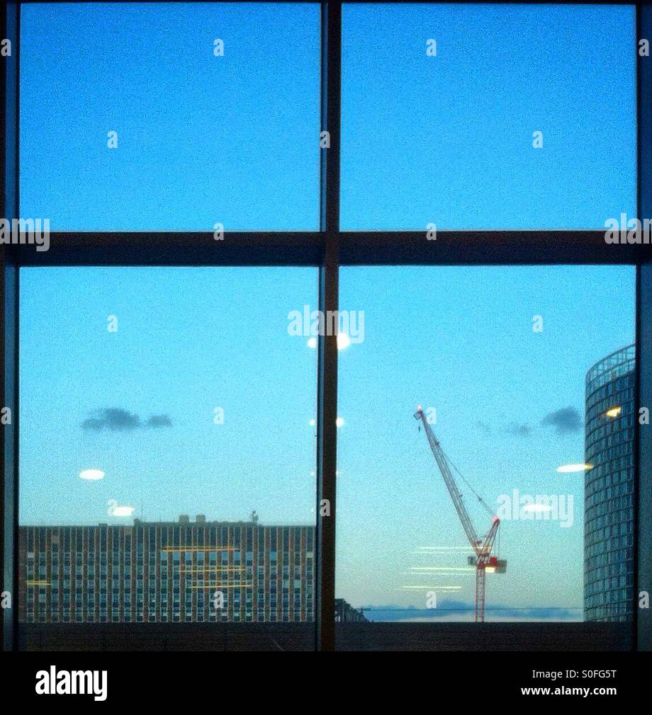 Blick auf London Gebäude und ein Kran durch ein Fenster in der Dämmerung Stockfoto