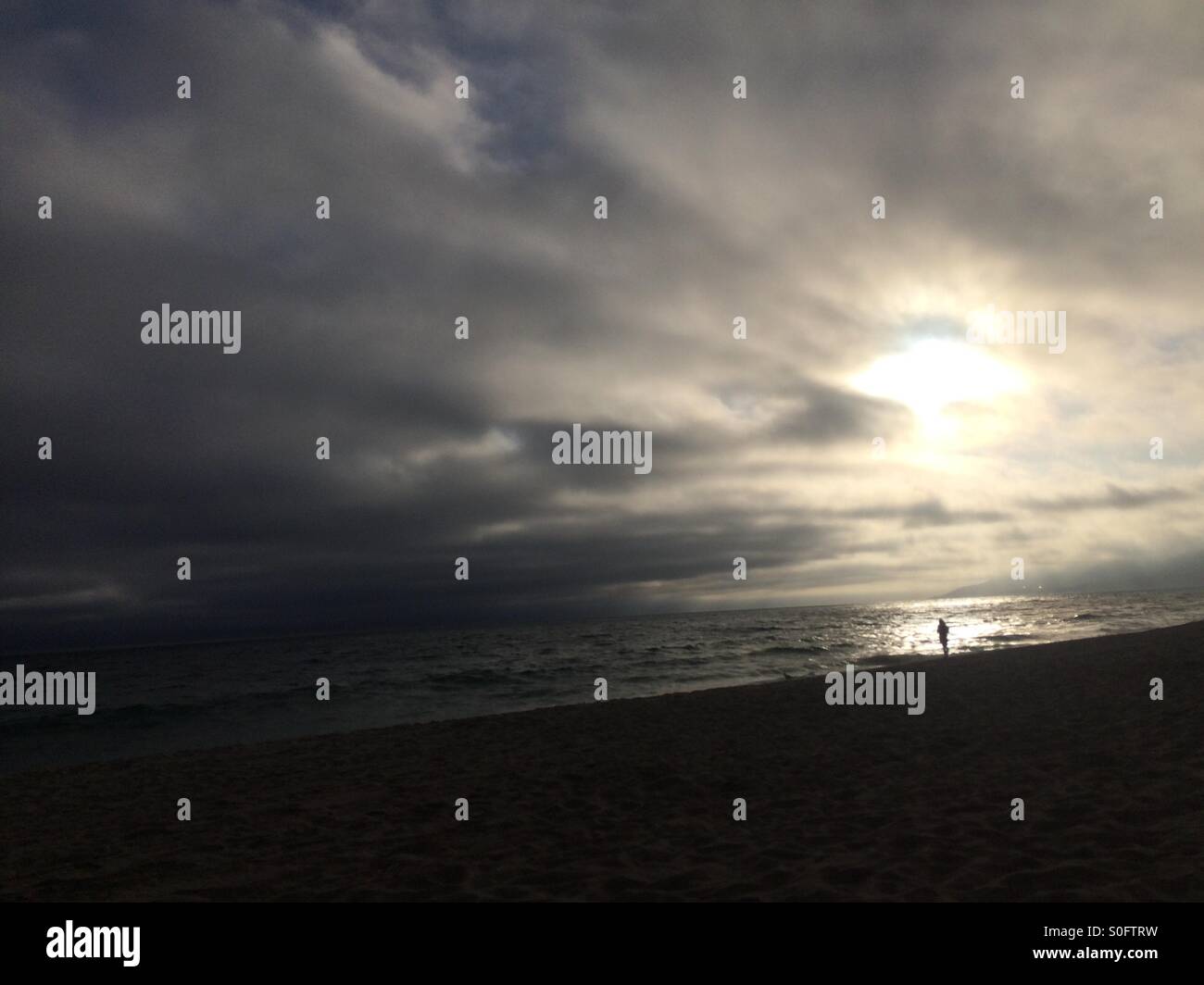 Eine einsame Gestalt betrachtet den Blick aufs Meer an einem Strand California als die Sonne untergeht. - Smartphone-aufgenommenes Stockfoto