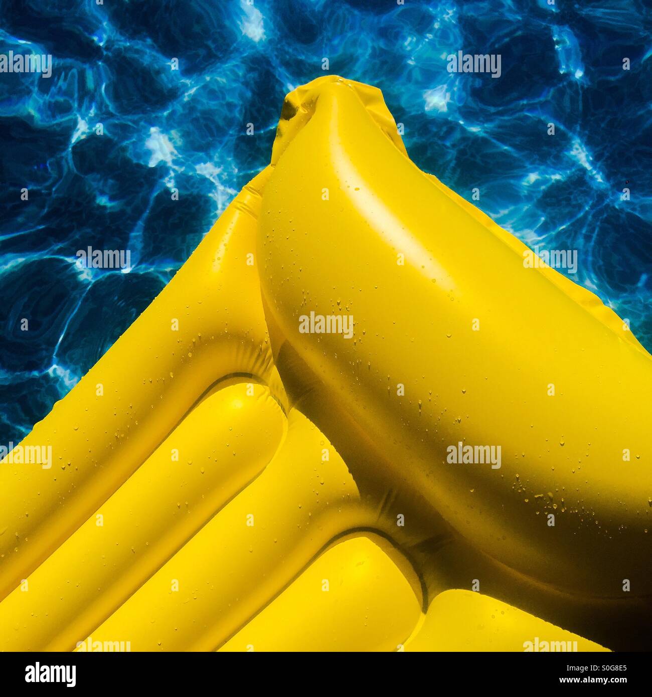Nahaufnahme der helle gelbe aufblasbare Matte schwimmt auf blauen Wassern des Swimming Pool in der Sonne. Stockfoto