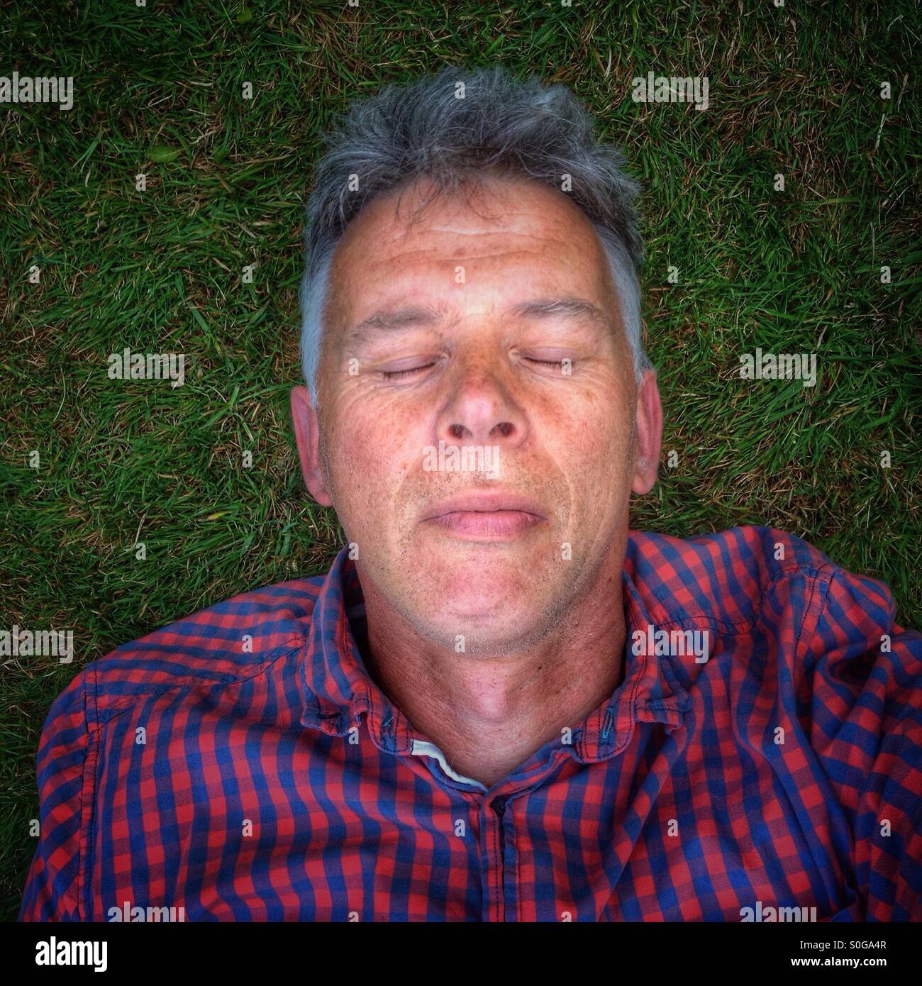 Mann mit geschlossenen Augen auf dem Rasen liegen. Stockfoto