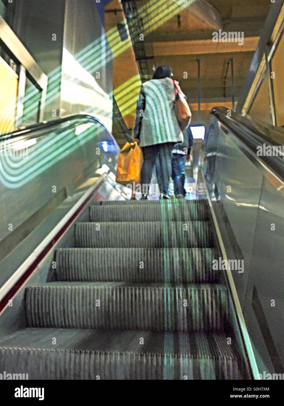 Linien des Reisens. Frau mit Tasche auf der Rolltreppe in die u-Bahnstation. - Smartphone-aufgenommenes Stockfoto
