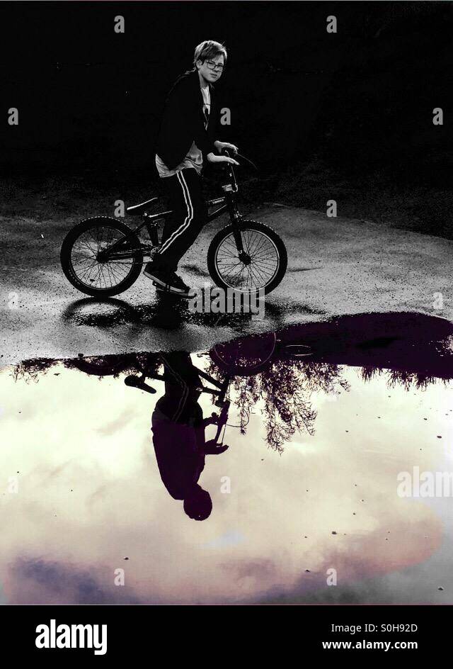 Junge Person sitzt weiter zu eine Pfütze auf seinem BMX-Rad mit dem Wasser sein Bild wie ein Spiegel reflektiert Stockfoto