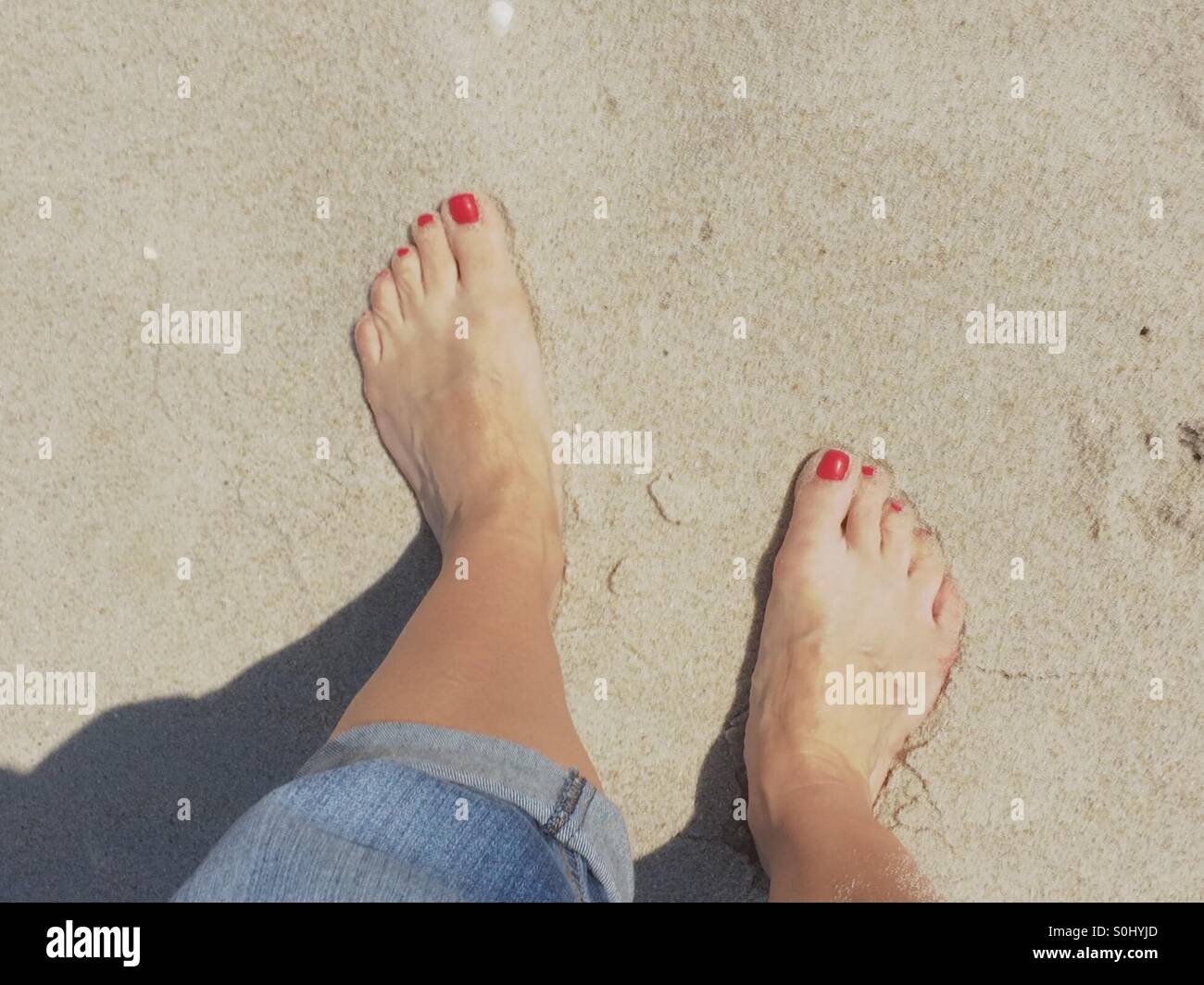 Füße mit roten Nägeln im sand Stockfoto