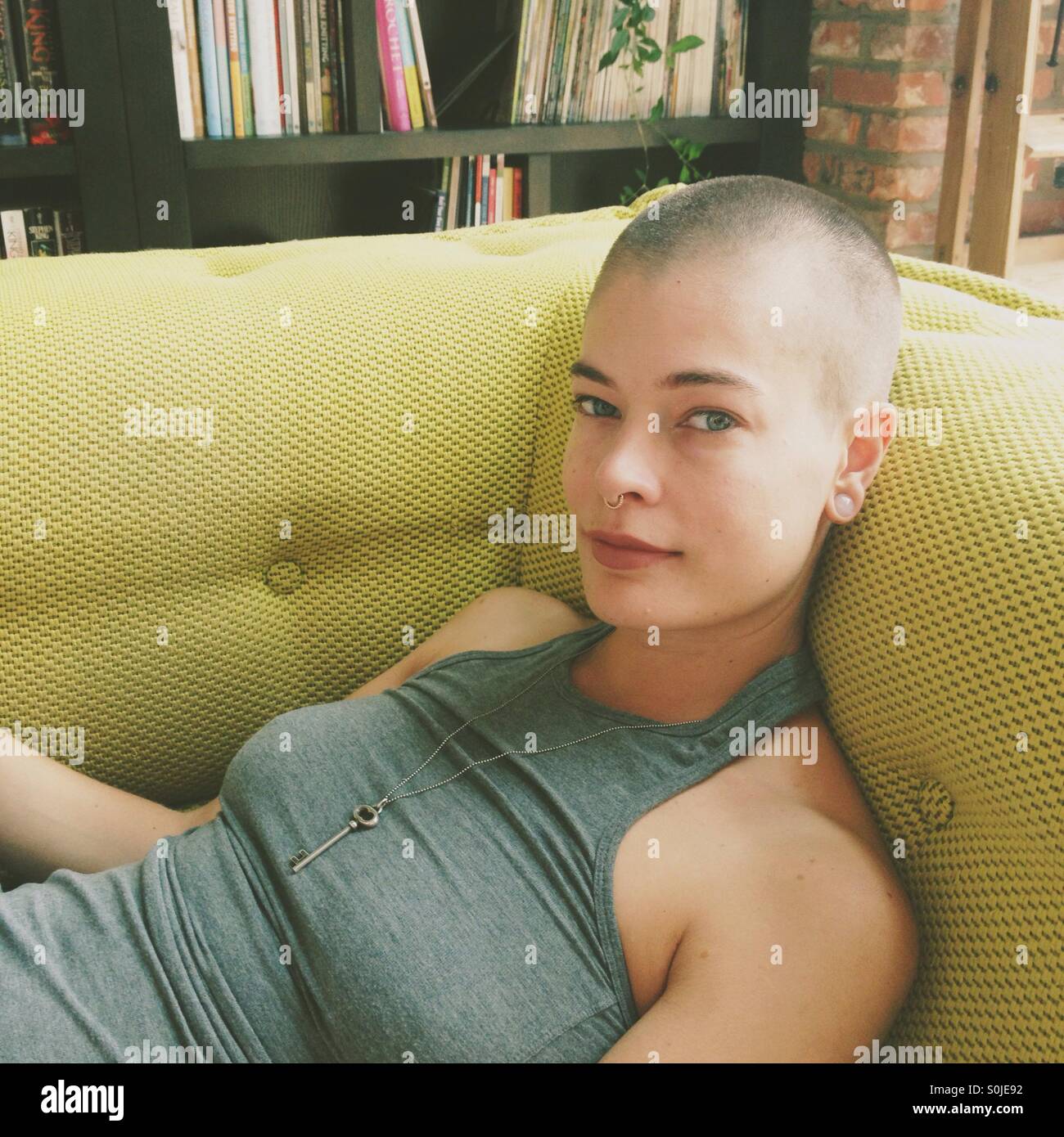 Frau mit rasierten Kopf lounges auf high-End-Mah-Jong-Sofa in einer Bibliothek Stockfoto