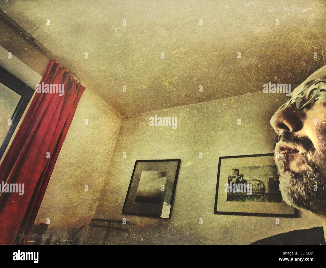 Depressiver Mann starrte aus dem Fenster in seinem Haus. - Smartphone-aufgenommenes Stockfoto