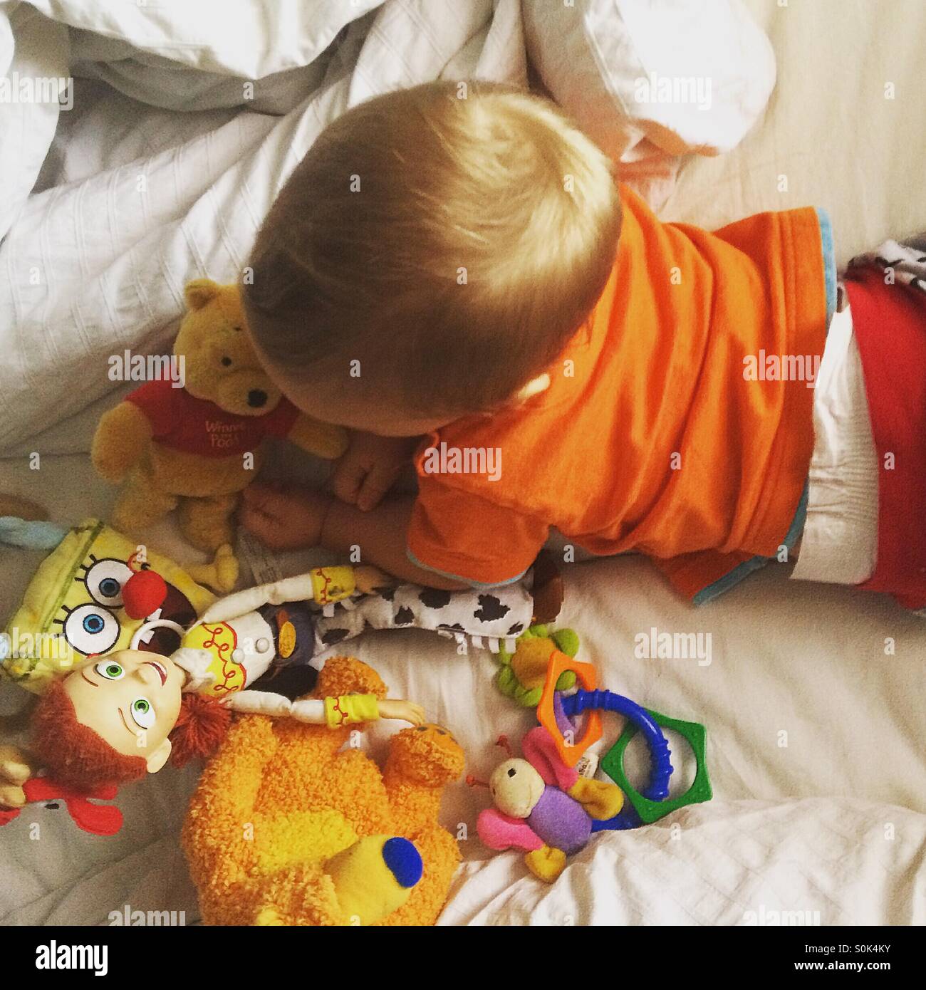 Baby Junge liegend auf dem Bauch im Bett seiner Eltern, Morgen Zeit spielt mit seinen Spielsachen Stockfoto