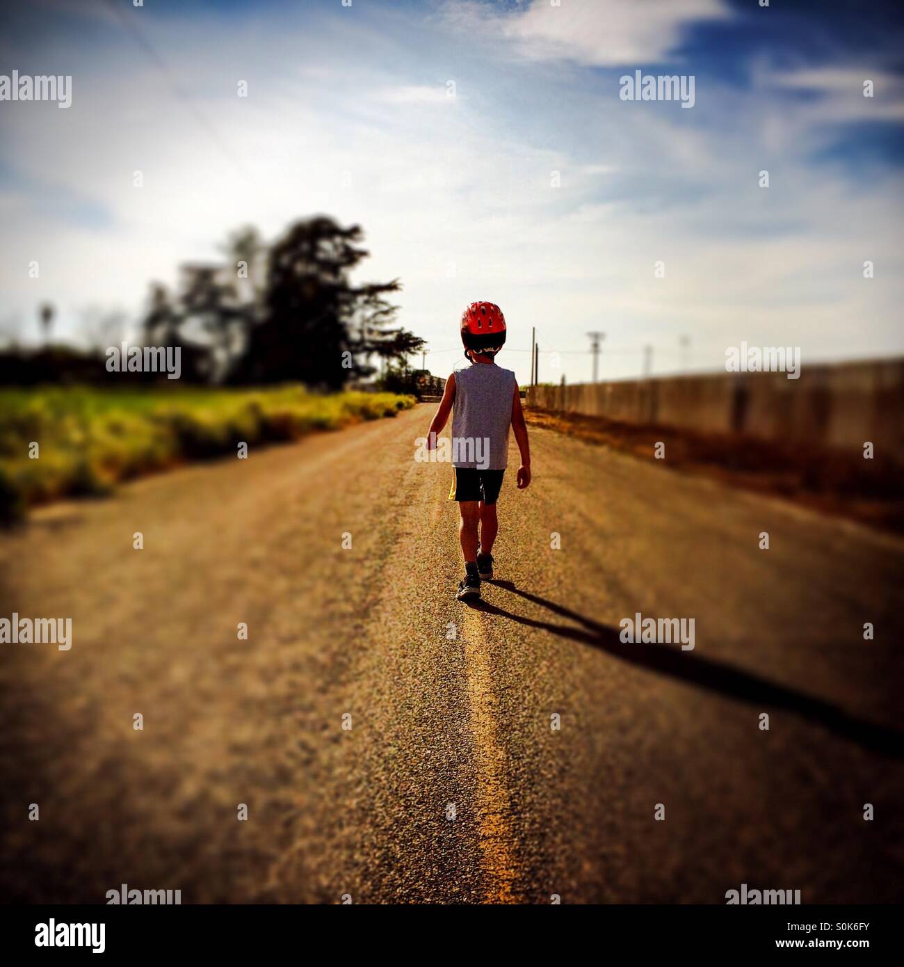 Ein 7 Jahre alter Junge läuft hinunter die Mitte einer Landstraße mit seinem Fahrradhelm. - Smartphone-aufgenommenes Stockfoto