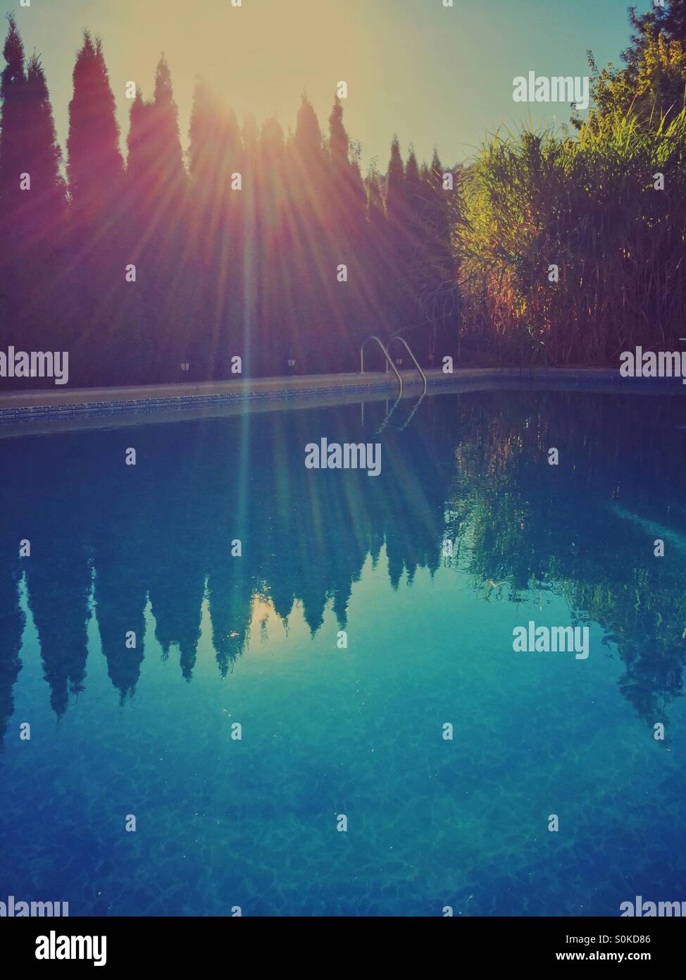 Abend am Pool. Spätsommer Sonnenuntergang leuchtet auf das blaue Wasser des einen leeren Hinterhof-Pool. Stockfoto