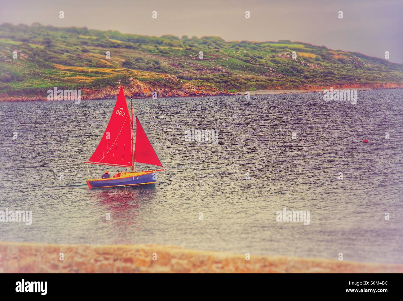 Ein rotes Segelboot mit einem einsamen Seemann begibt sich auf das Meer. Stockfoto