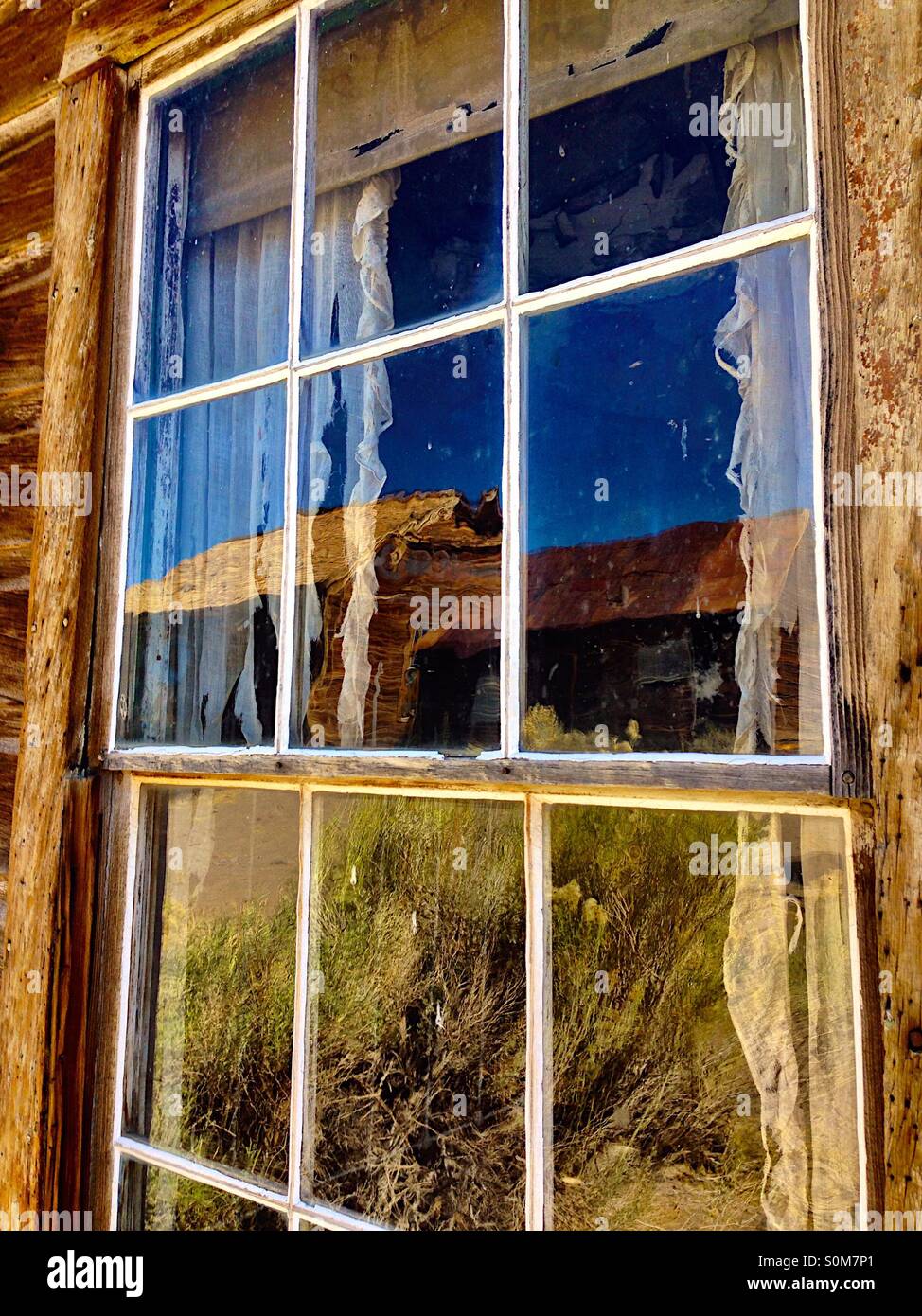 Alte Holzbauten spiegelt sich in einem alten Fenster - Smartphone-aufgenommenes Stockfoto
