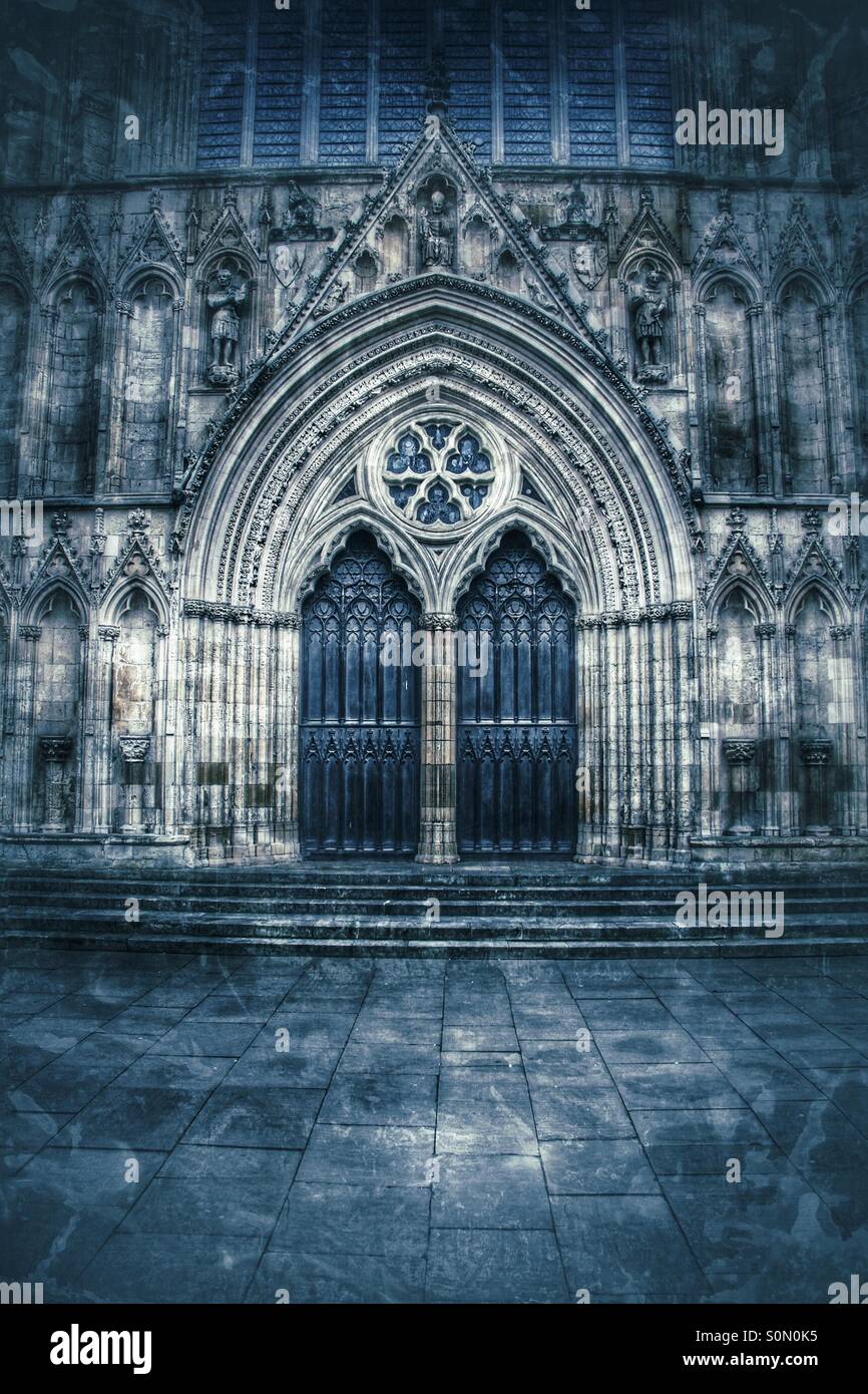 Die abgedunkelten Türen einer englischen Kathedrale. Kunstvolle Steinmetzarbeiten rund um Dicke Holztüren im York Minster. - Smartphone-aufgenommenes Stockfoto