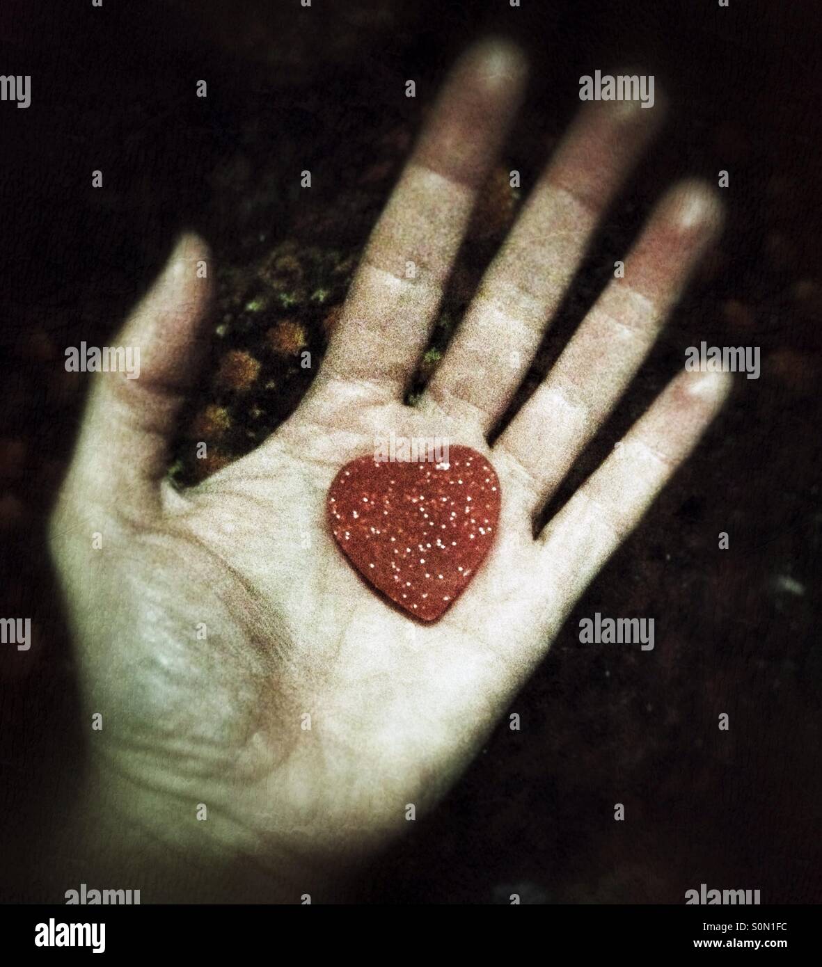 Die Hand einer Frau mit einem kleinen roten Herzen in ihrer Handfläche Stockfoto