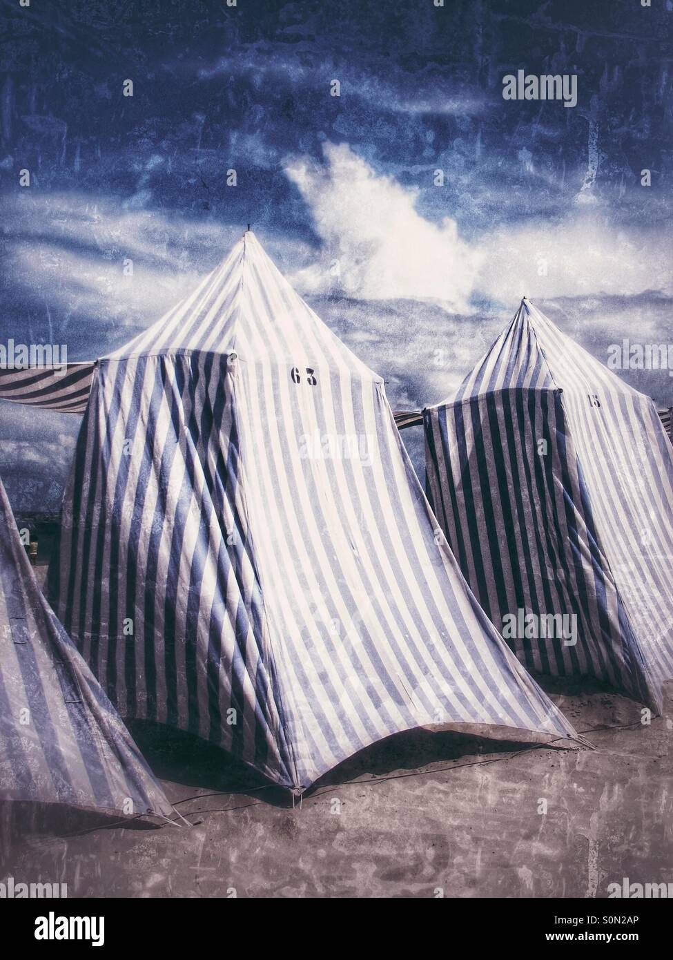 Blau und weiß gestreifte Strandzelte sitzen auf einem sandigen Strand für Urlauber bereit. - Smartphone-aufgenommenes Stockfoto
