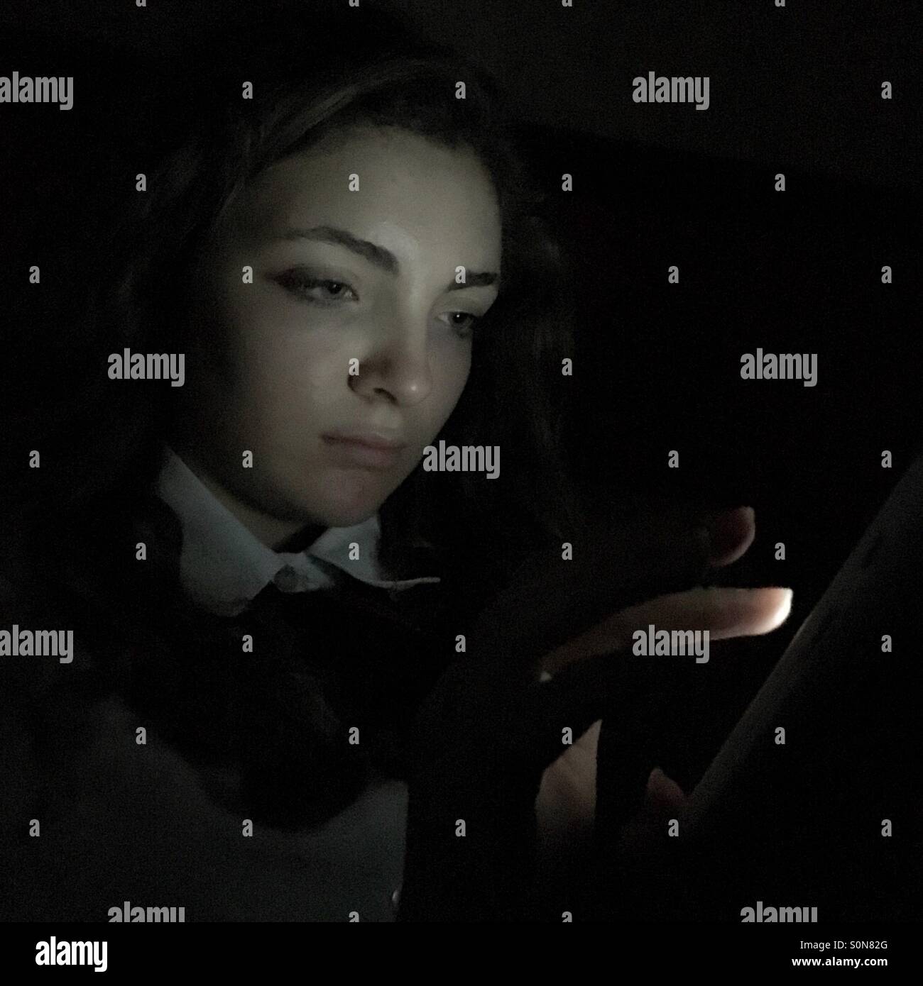 Ein junges Mädchen auf ihrem Mobiltelefon in einem dunklen Raum Stockfoto