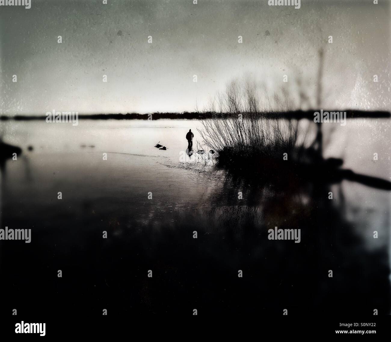 Eine dunkle, geheimnisvolle Gestalt steht in einem See mit Winternebel steigt aus dem Wasser Stockfoto