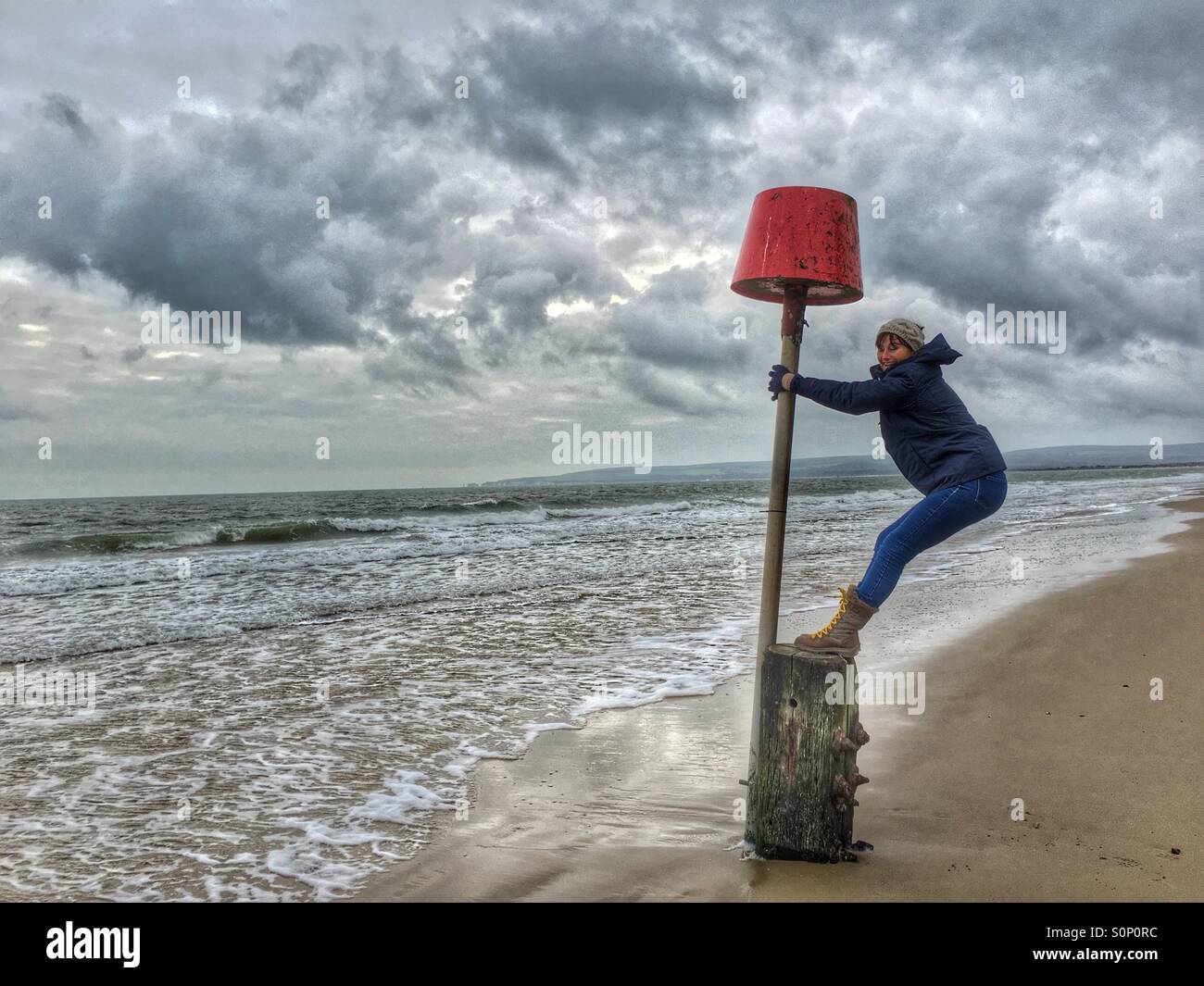 Frau mit Spaß balancieren auf Markierungsboje auf Dorset Strand im Winter Stockfoto