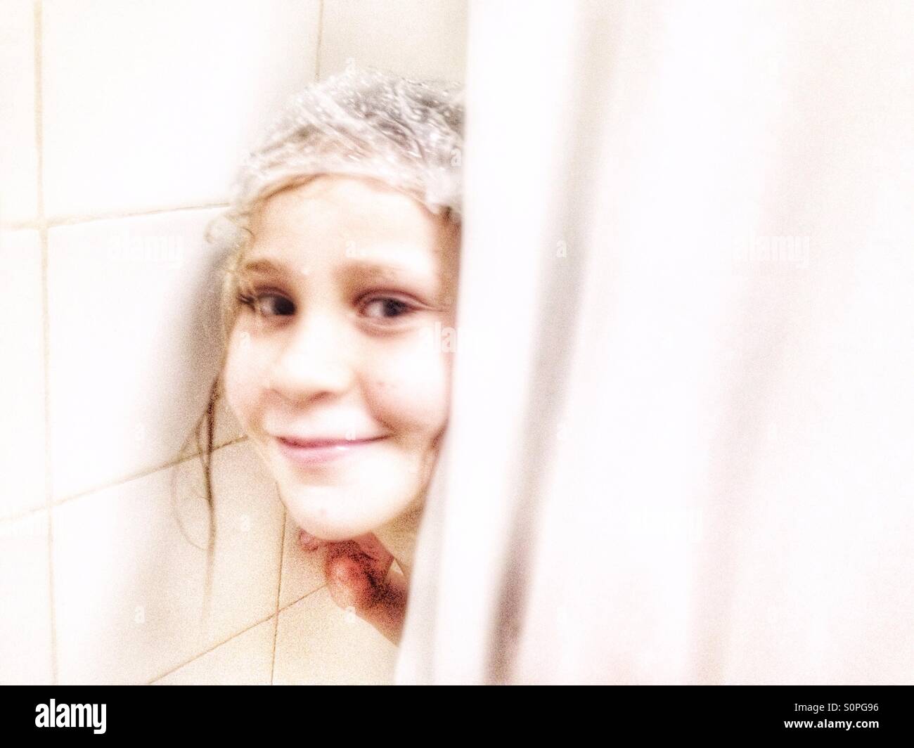 Junge Mädchen tragen eine Duschhaube versteckt sich hinter einem Duschvorhang. Stockfoto