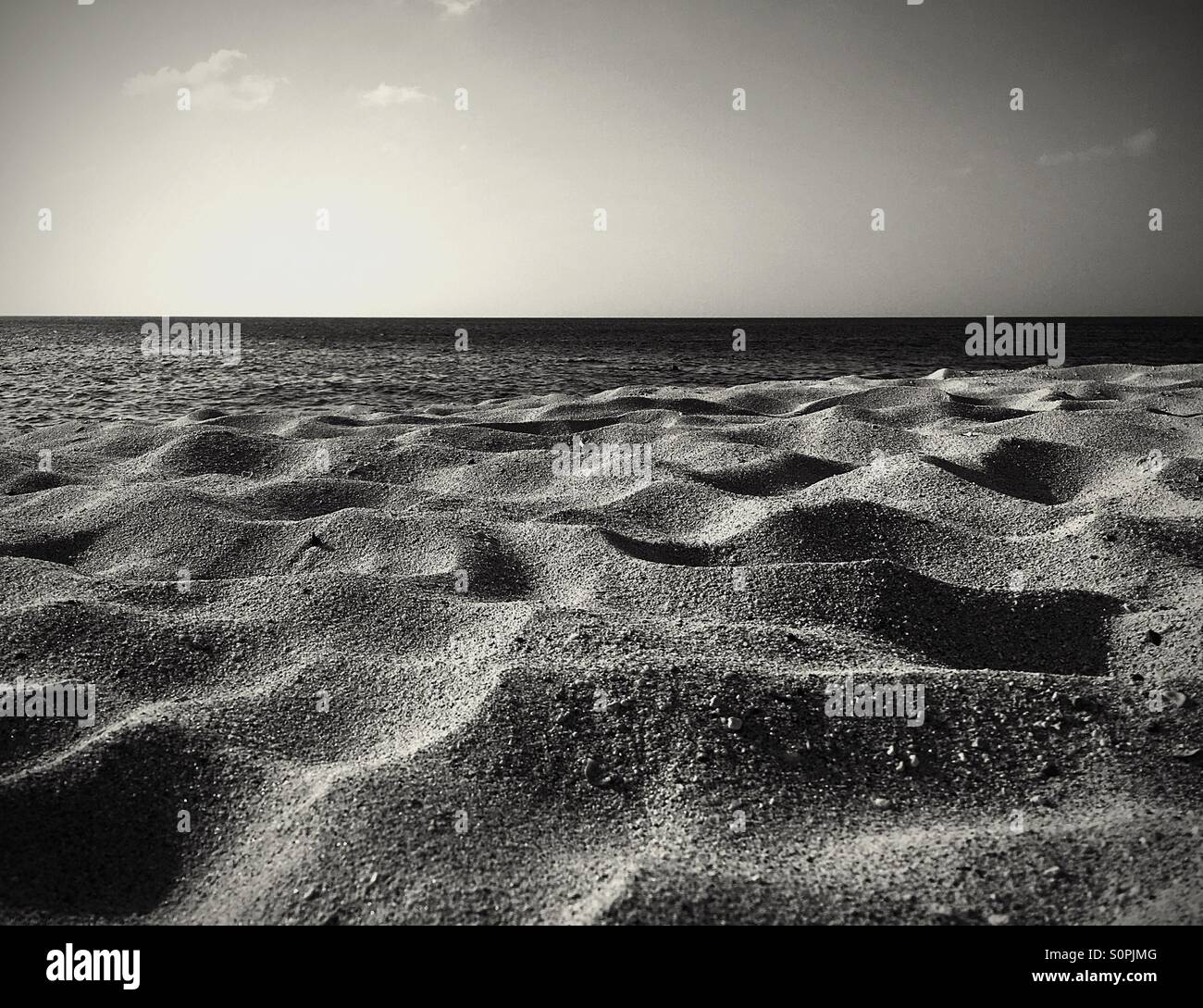 Wellen im Sand mit dem Ozean im Hintergrund in schwarz und weiß - Smartphone-aufgenommenes Stockfoto