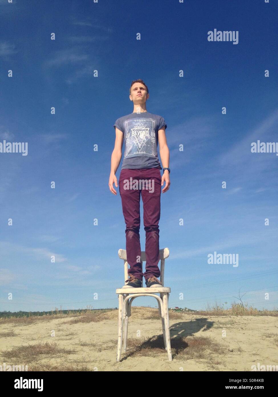 Mann in Hemd und Hose auf einem Stuhl auf dem Hügel, die ernsthaft auf der Suche in die Ferne auf blauen Himmelshintergrund Stockfoto