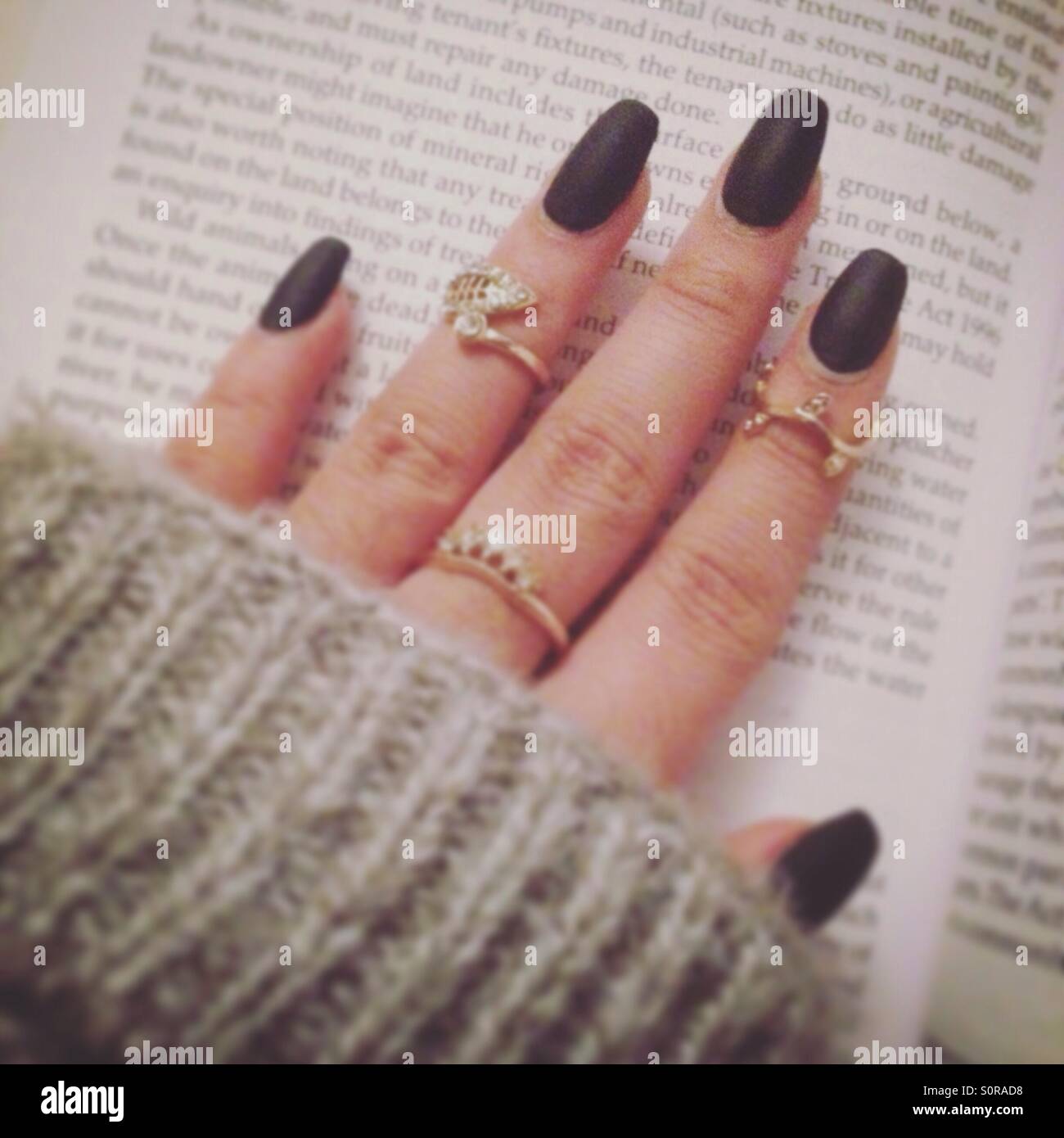 Matt schwarze Nägel mit MIDI-Ringen in w grauen Pullover, während ein Buch  zu lesen Stockfotografie - Alamy
