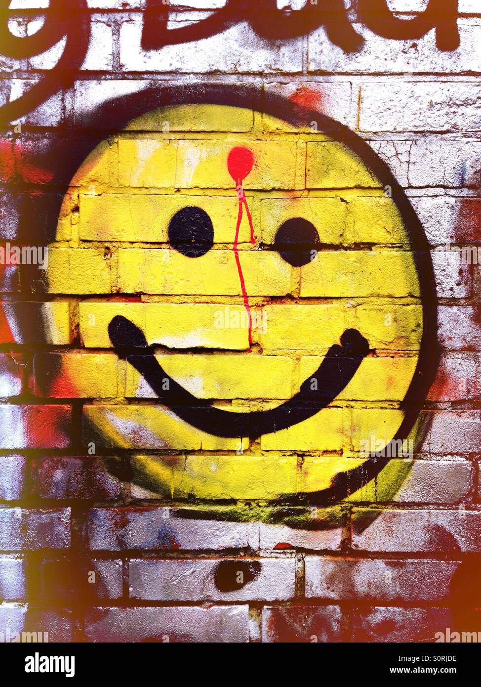 Smiley-Graffiti mit einem roten Fleck auf der Stirn Stockfoto