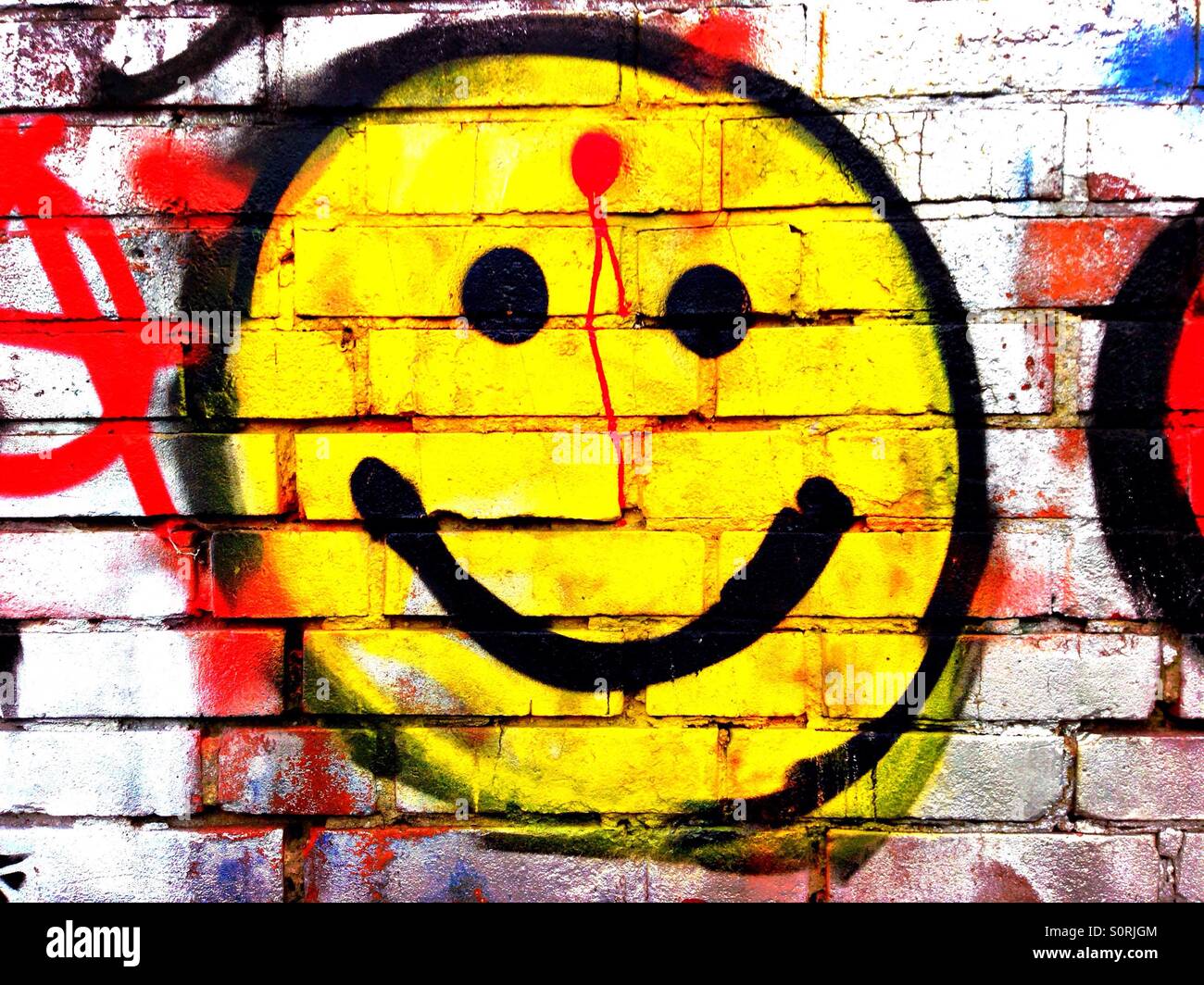 Smiley-Graffiti mit einem roten Punkt auf der Stirn, wie eine Schusswunde Stockfoto
