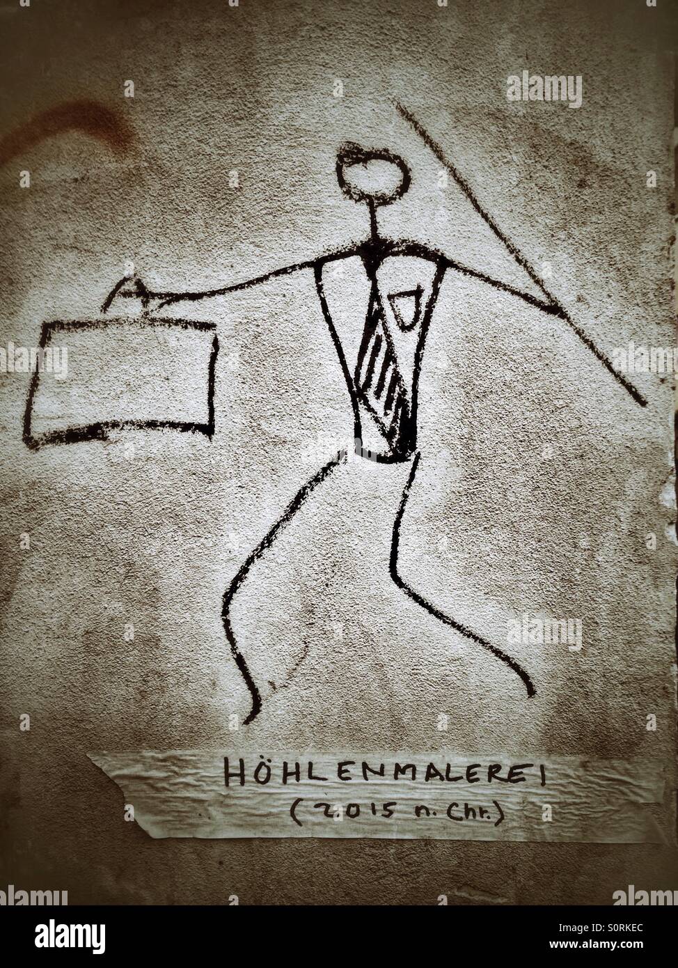Ein Graffiti von einer modernen Höhlenmenschen mit Aktenkoffer und Speer, deutsche Untertitel liest: Höhle, Malerei (2015 n. Chr.) Stockfoto
