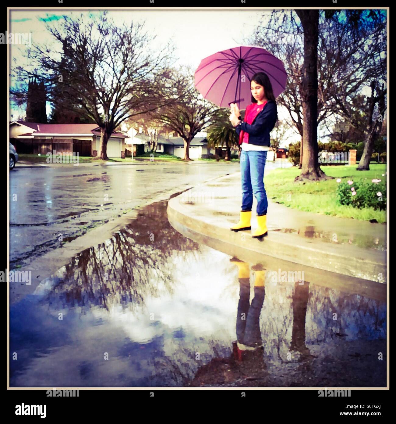 Ein 12 Jahres altes Mädchen mit Regen Stiefel und Regenschirm als Regen aufräumt. Stockfoto