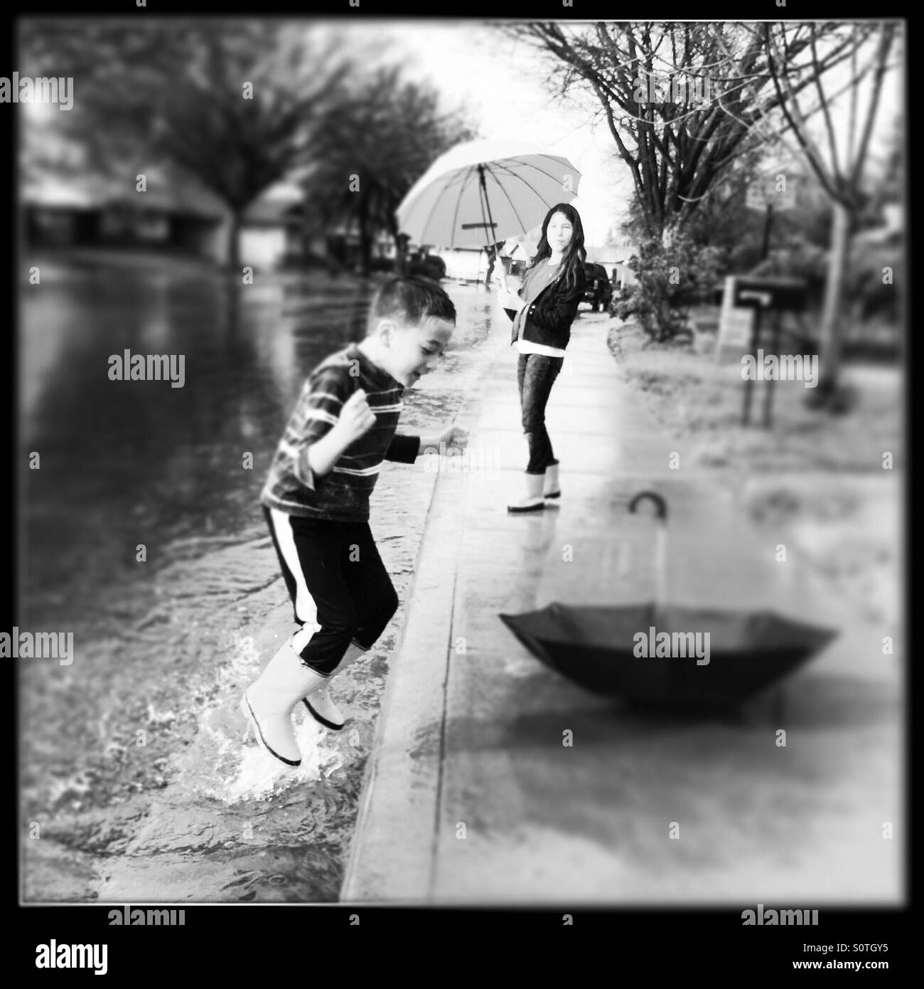 Ein 12 Jahre altes Mädchen und ihrem 7-jährigen Bruder draußen im Regen spielen. Stockfoto