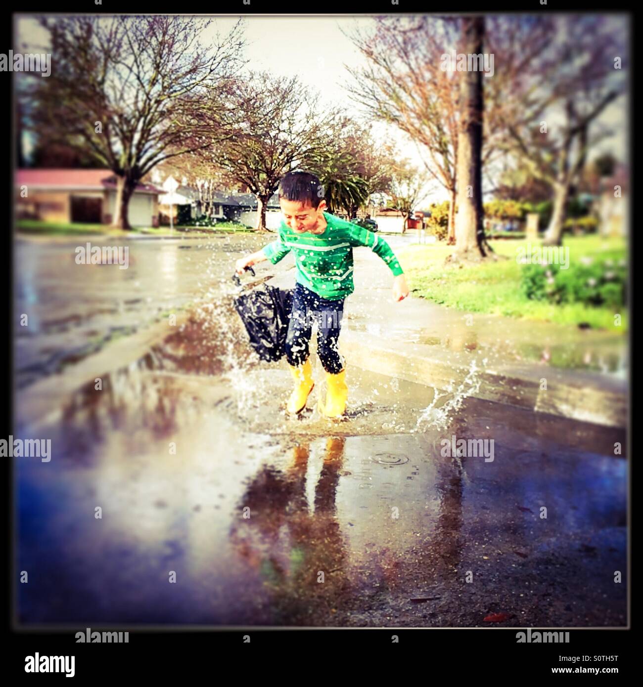 Ein 7 Jahre alter Junge springt in eine Pfütze mit seinem Regenstiefel auf. Stockfoto