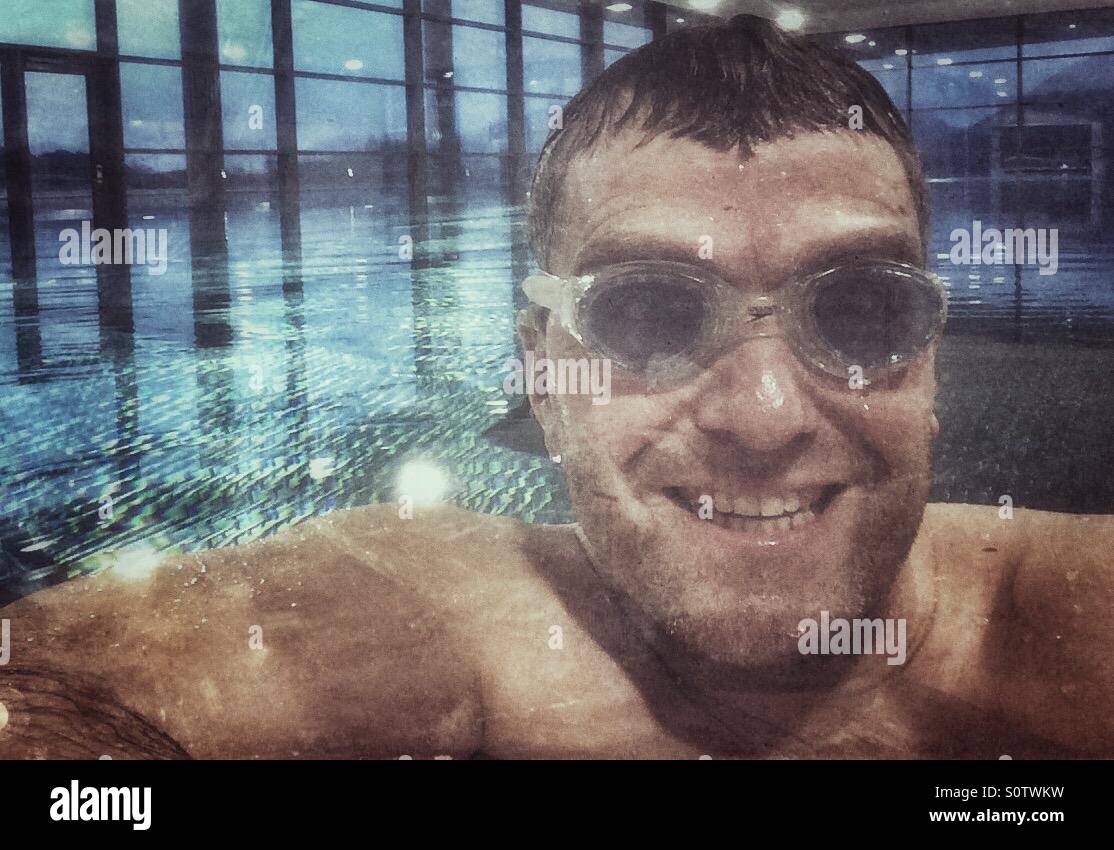 Lächelnd Mitte im Alter Mann mit Brille am Rande des drinnen schwimmen schwimmen Pool. Stockfoto