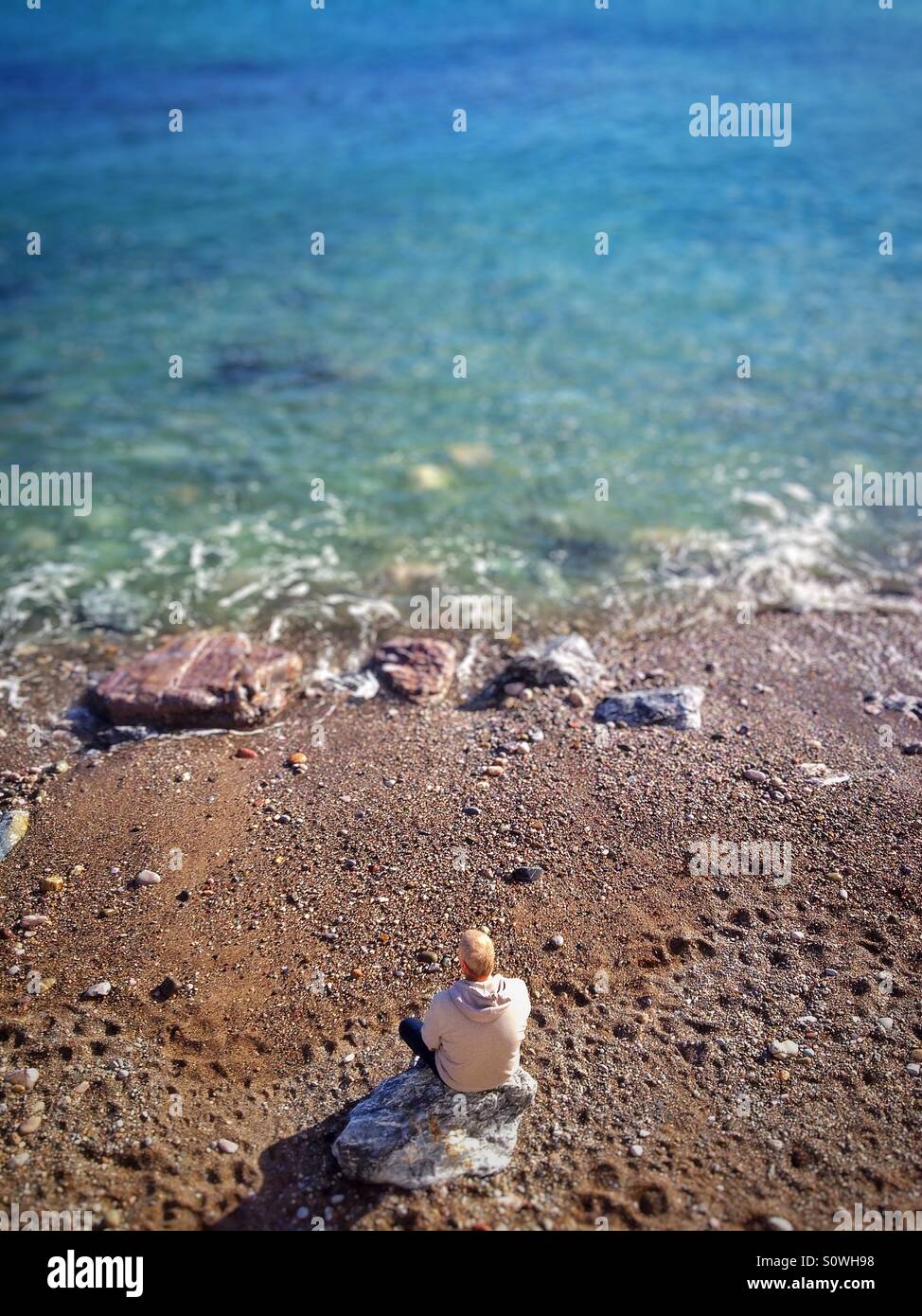 Mann, sitzend auf Felsen, Blick auf das Meer Stockfoto