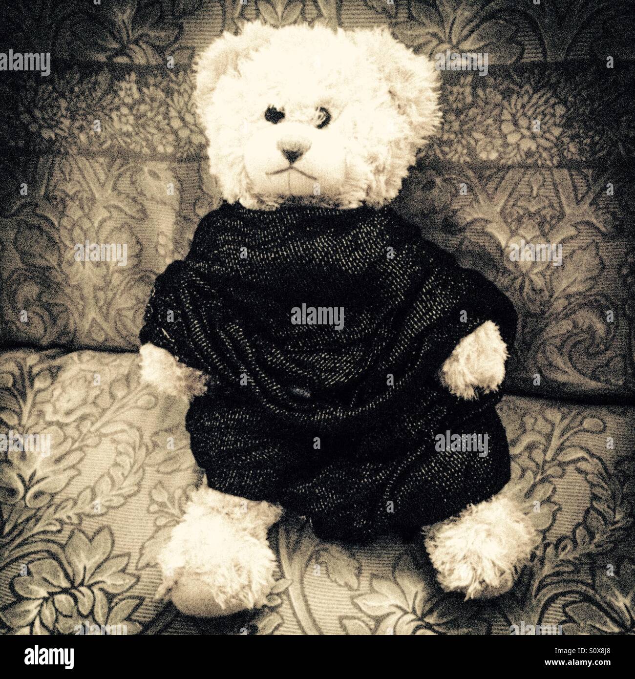 Weißer Teddybär in einem schwarzen Kleid auf dem Sofa sitzen Stockfoto
