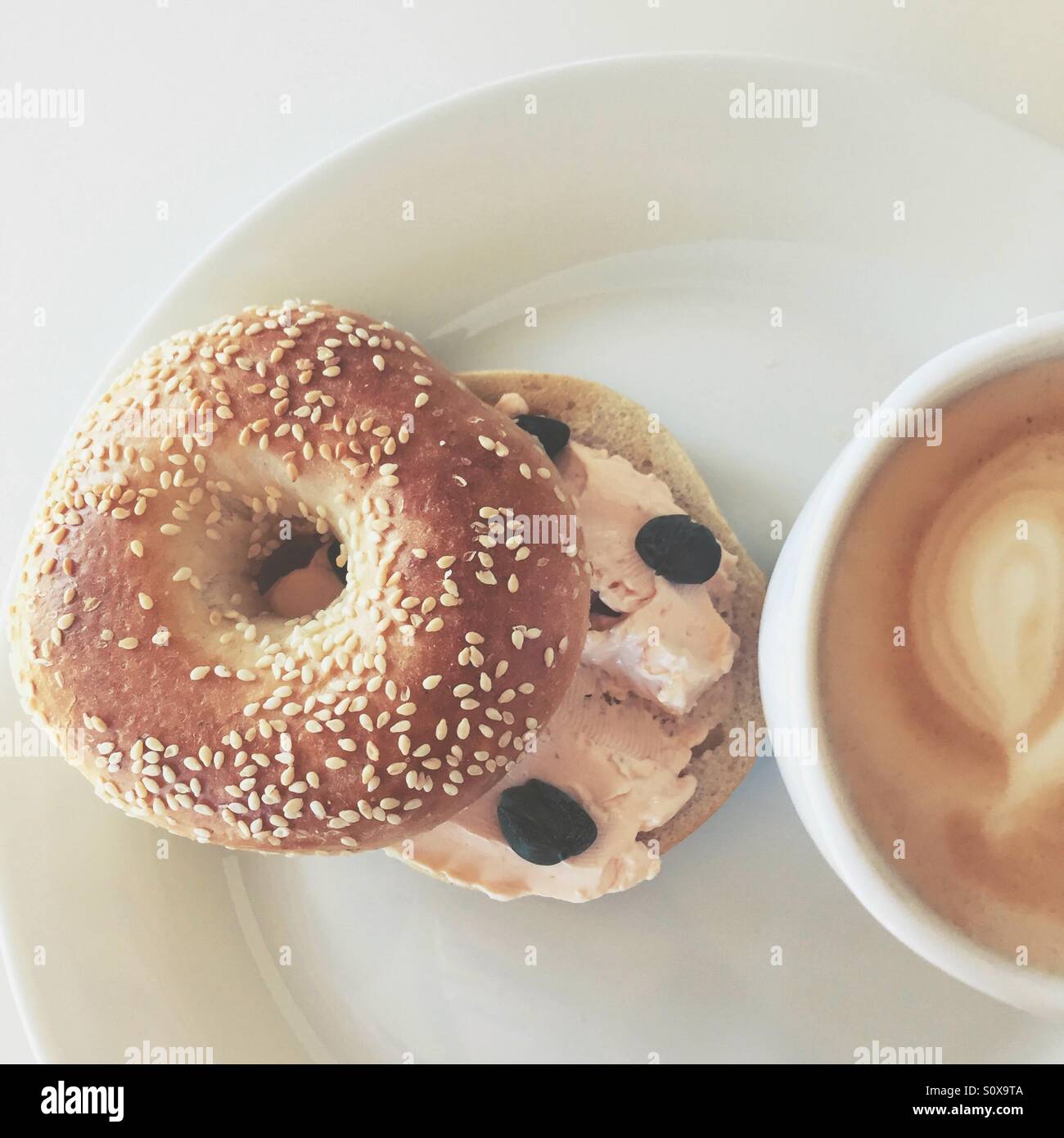 Geräucherter Lachs mit Frischkäse, Kapern in Sesam Bagel und eine Tasse Latte. Stockfoto