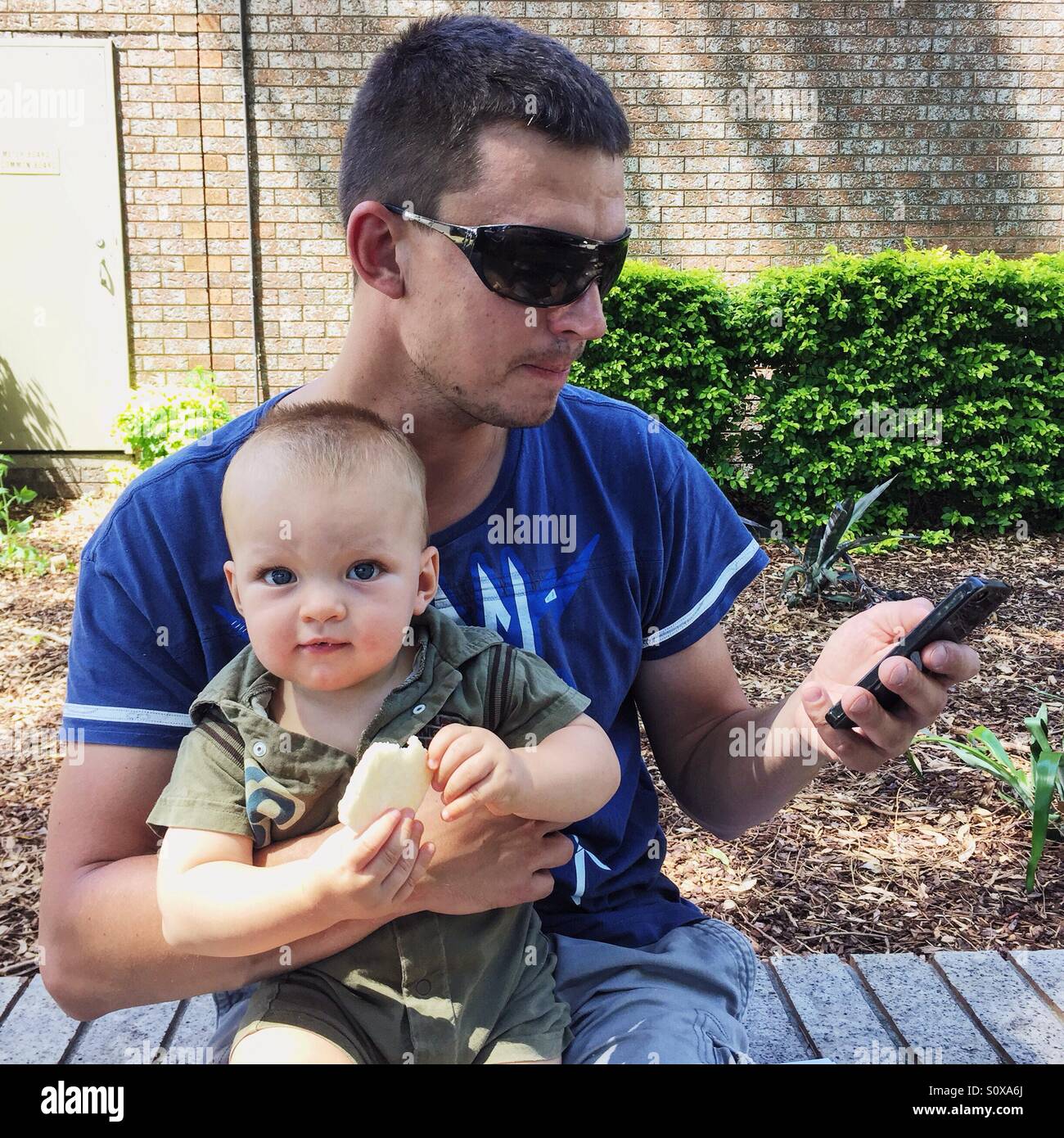 Vater Holding Baby und Blick auf Handy Stockfoto