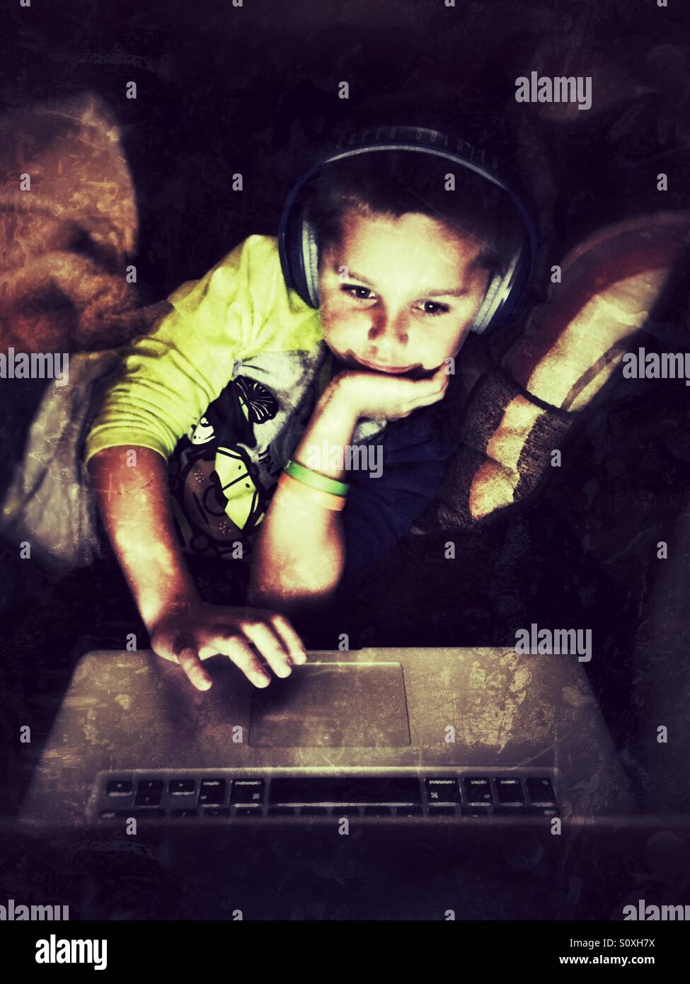 Kleiner Junge mit Kopfhörern verwendet einen laptop Stockfoto