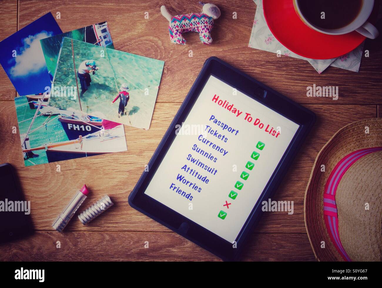 Eine Wohnung lag Tischplatte mit einem "Aufgabenliste" auf einem Tablet, als eine Person ihre Ferien oder Urlaub organisiert. Blick von oben auf einen belebten Schreibtisch mit Elementen, die im Zusammenhang mit Reisen und Urlaub auf sie. - Smartphone-aufgenommenes Stockfoto