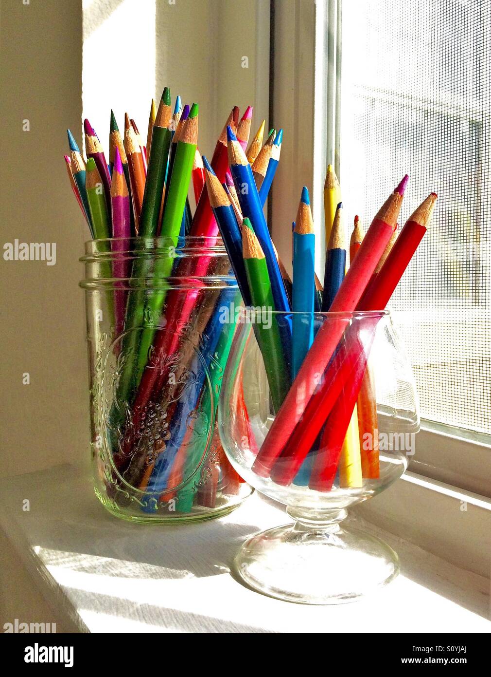 Eine Auswahl an Buntstiften in Glasbehältern sitzt auf einer sonnigen Fensterbank Stockfoto