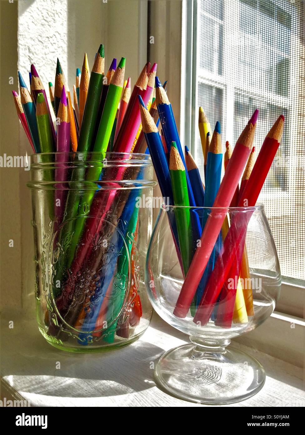 Eine Auswahl an Buntstiften sitzen in Glasbehältern auf einer sonnigen Fensterbank Stockfoto