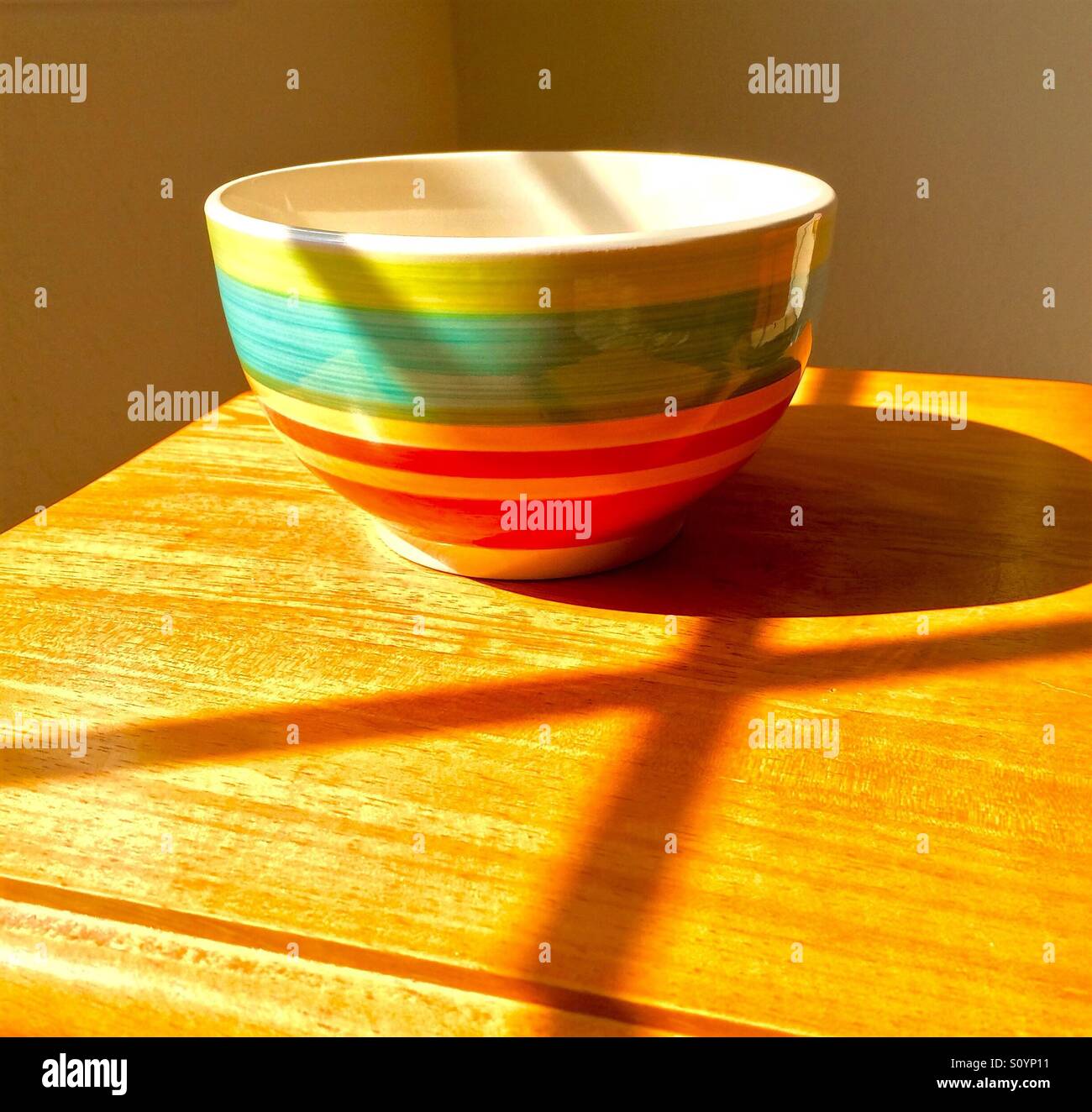 Bunte Schale auf Holztisch mit dramatischen Schatten - Smartphone-aufgenommenes Stockfoto