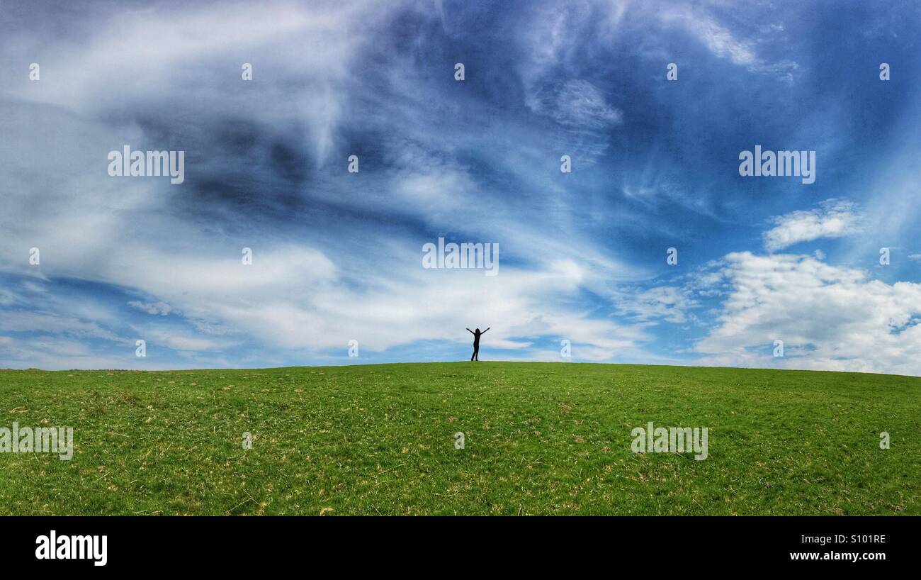 Silhouette Abbildung mit Armen hoch gehalten, am Horizont der sanft hügeligen Wiese bedeckt und blauer Himmel - Smartphone-aufgenommenes Stockfoto
