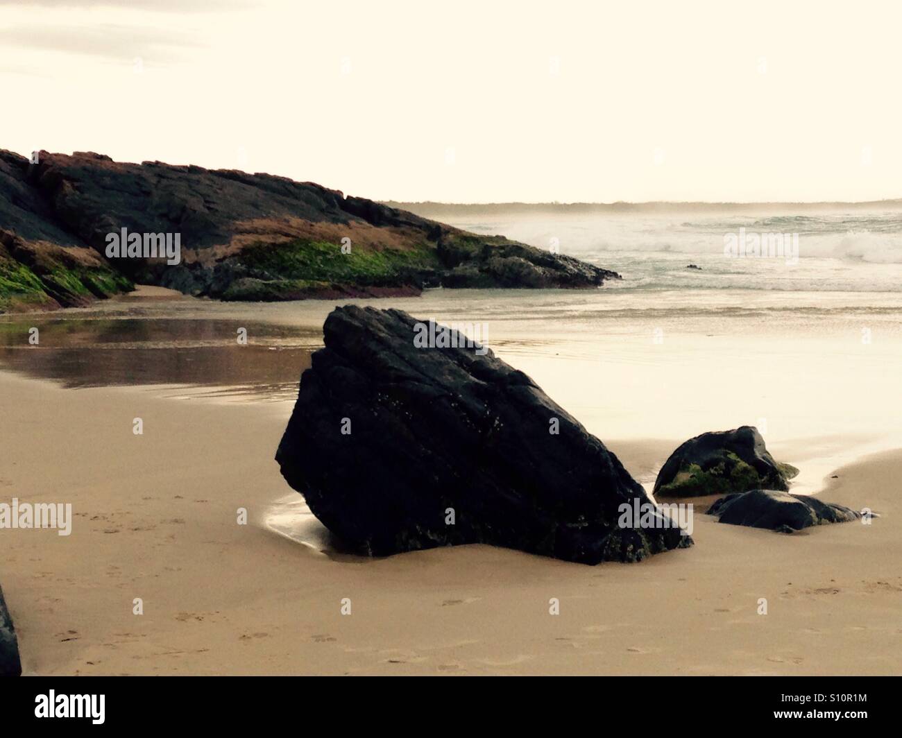 Robuste Rock von der Strandseite, die Kraft der sanften Wellen tragen Weg an einem unerschütterlichen Felsen im Laufe der Zeit, Geduld. Stockfoto