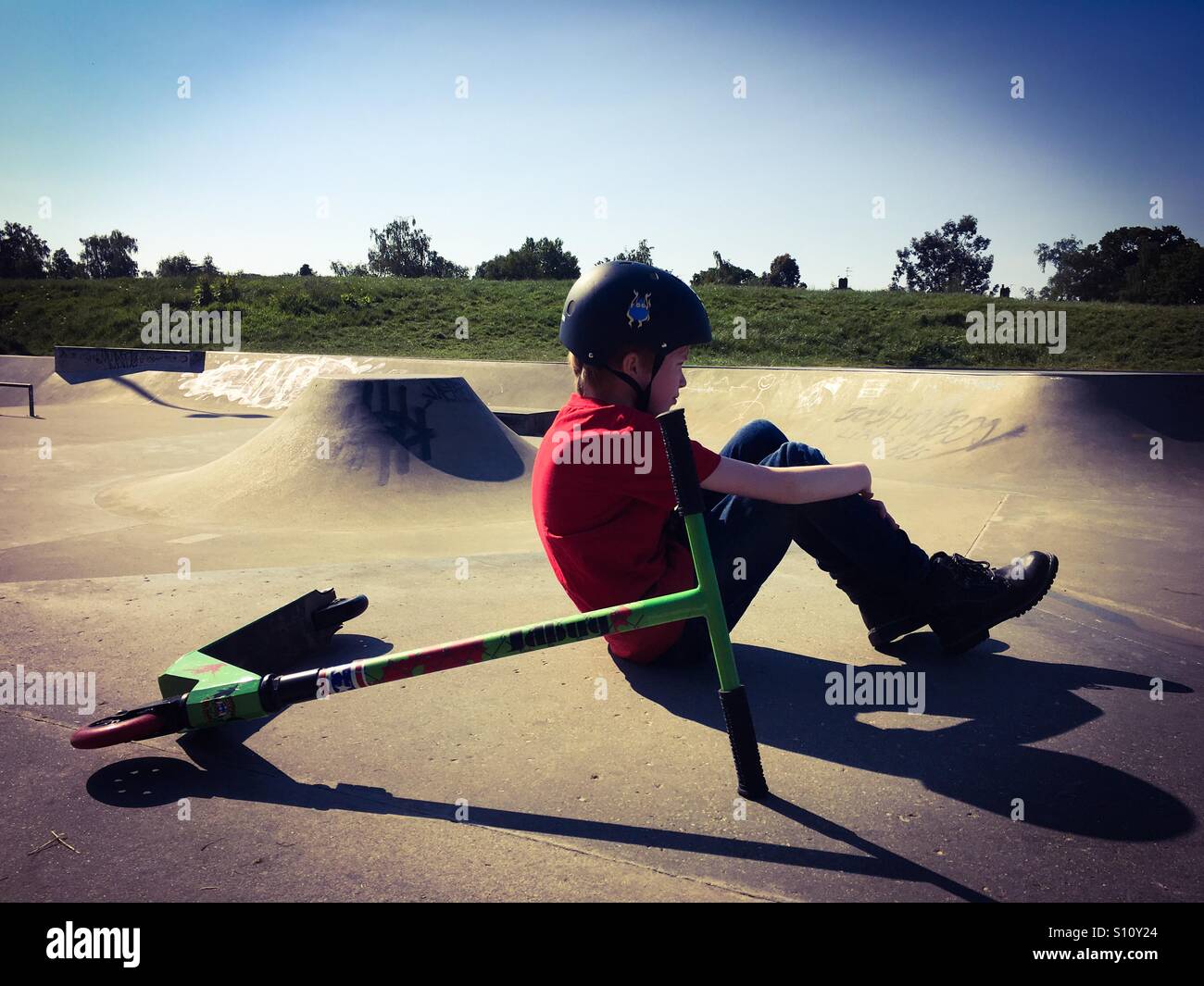 Ein 9-jähriger Junge sitzt mit seinem Roller Eaton Park Skatepark in Norwich, Großbritannien Stockfoto
