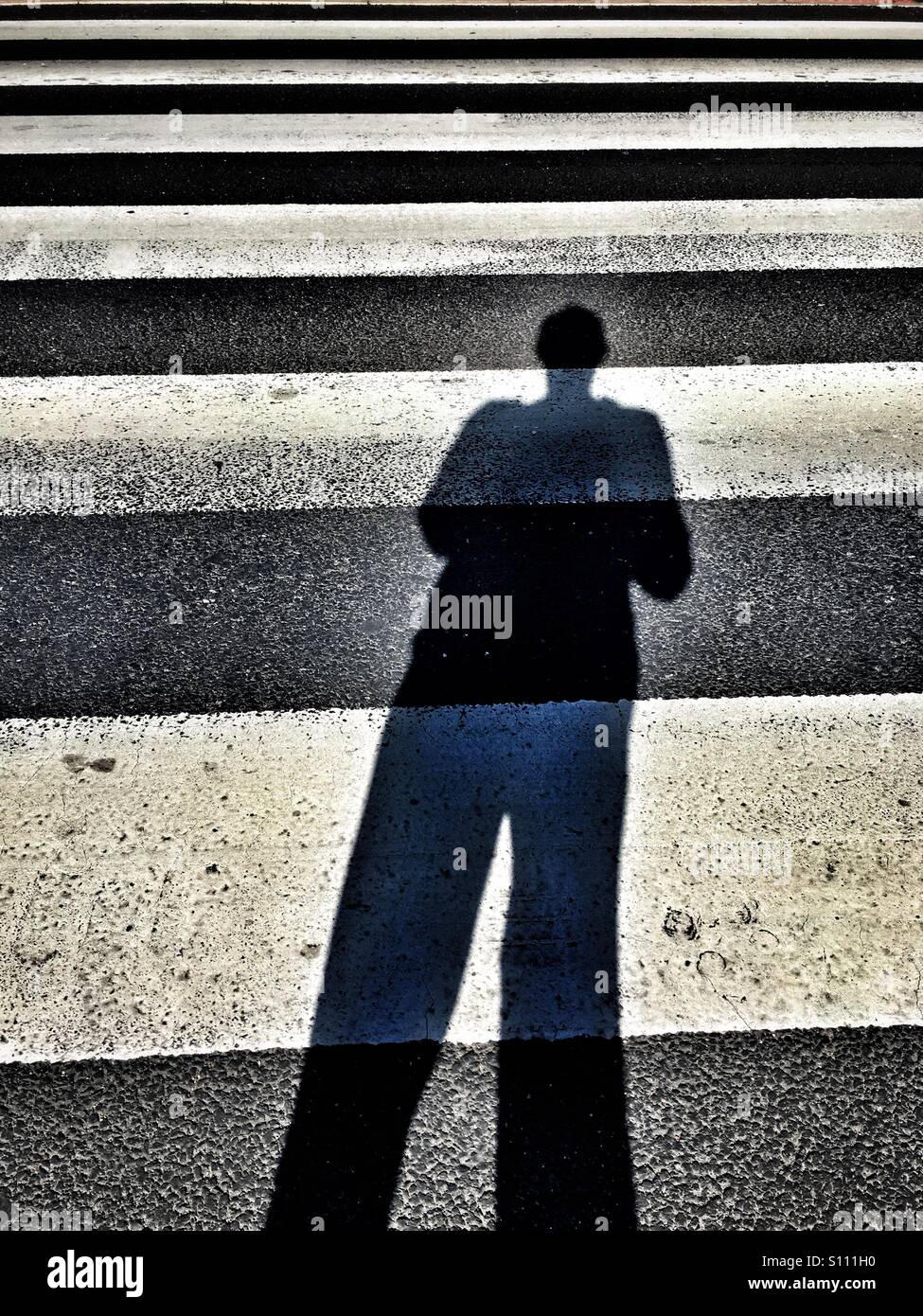Schatten des Mannes über Zebrastreifen Stockfoto