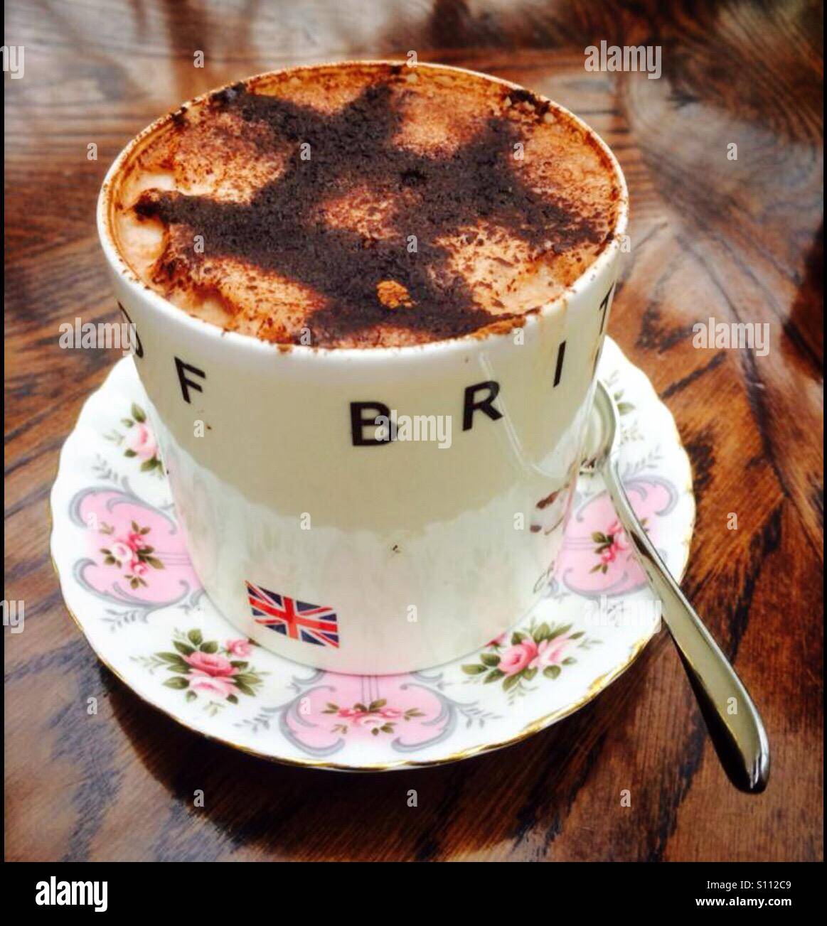 Tasse heiße Schokolade in eine dekorative Porzellan Tasse und Untertasse mit Löffel auf eine polierte Eiche Tisch Stockfoto