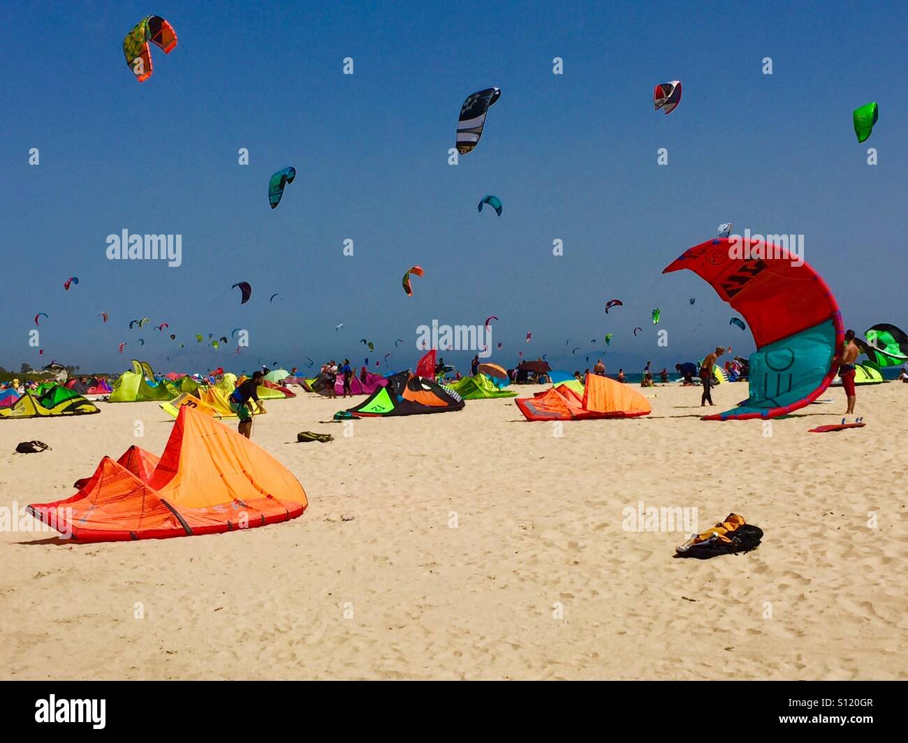 Farbenfrohe Kitesurfer an einem Sandstrand bei sonnigem Wetter - Smartphone-aufgenommenes Stockfoto