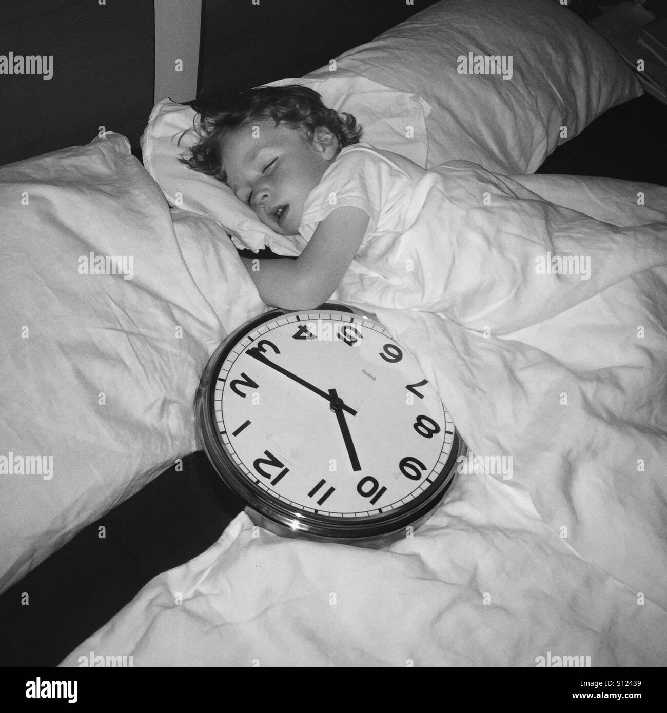 Junge, 5 Jahre schlafen im Bett mit einer großen Wanduhr, Deutschland Stockfoto