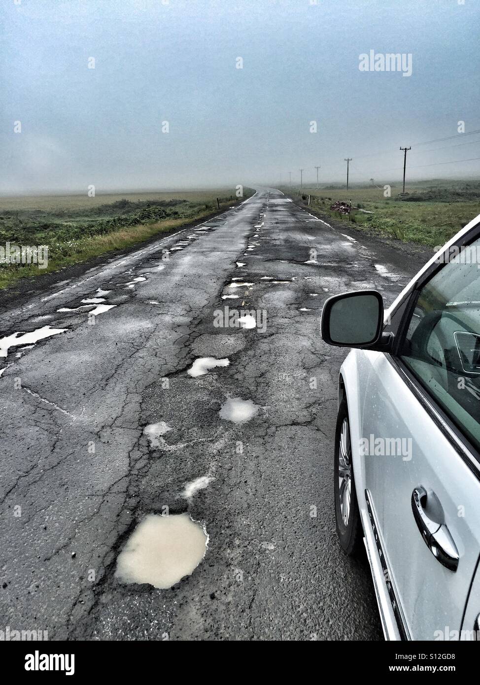 Ein Auto wird eine Schlagloch gefüllten sekundäre Autobahn beurteilt. Stockfoto