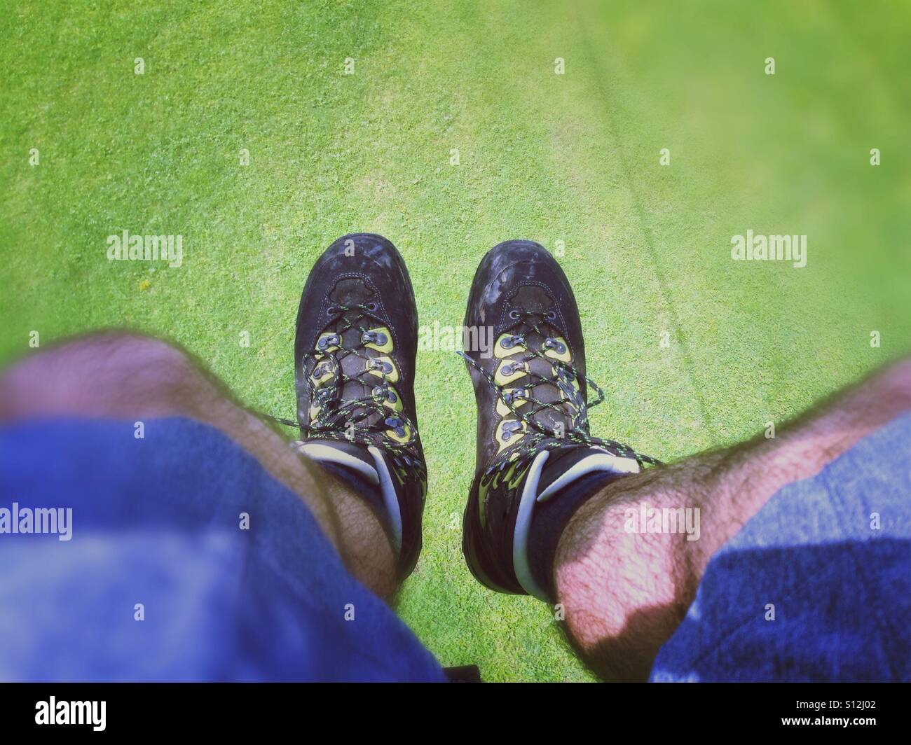 Männliche Füße mit Wanderschuhen in einem Sessellift über eine sehr grüne Wiese Stockfoto